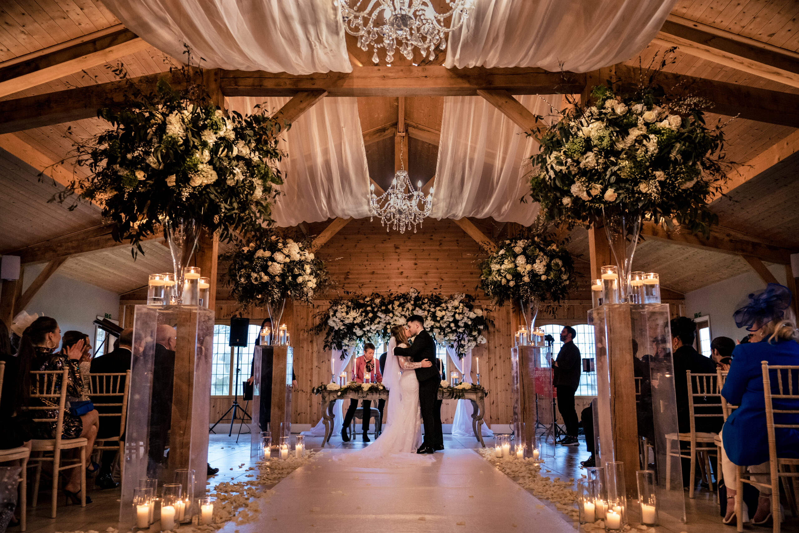 Wide view of the candlelit ceremony room at Merrydale Manor filled with white flowers by Red Floral