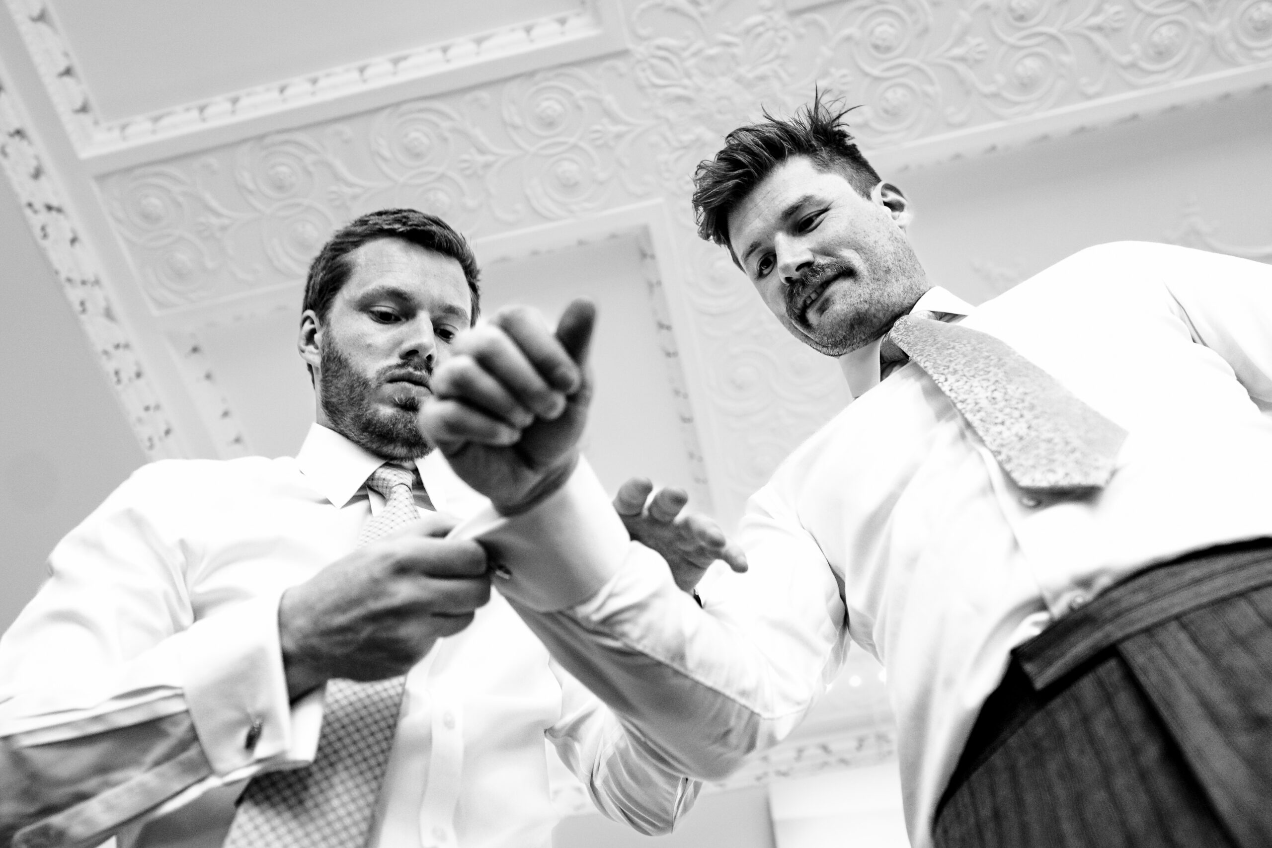Black and white photograph of groomsmen helping each other with cufflinks before the ceremony, Cheshire wedding photographer