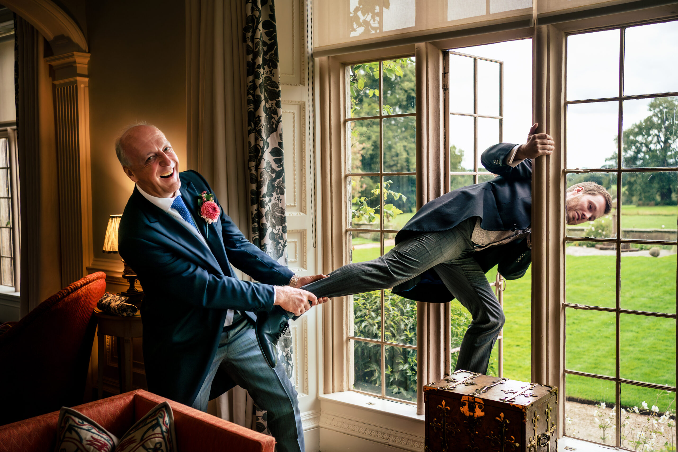 Groomsman swinging off a window frame while another laughs, morning of a Dorfold Hall wedding
