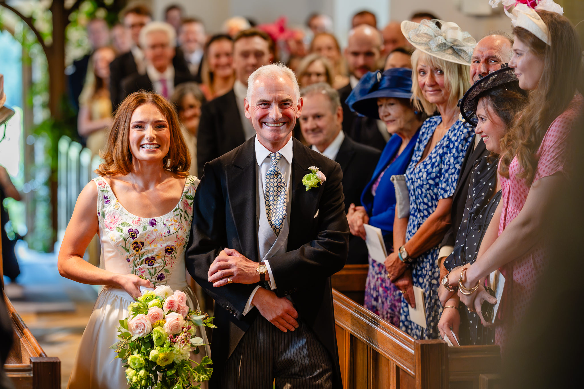 Bride walking down the aisle on her father’s arm as guests turn to watch