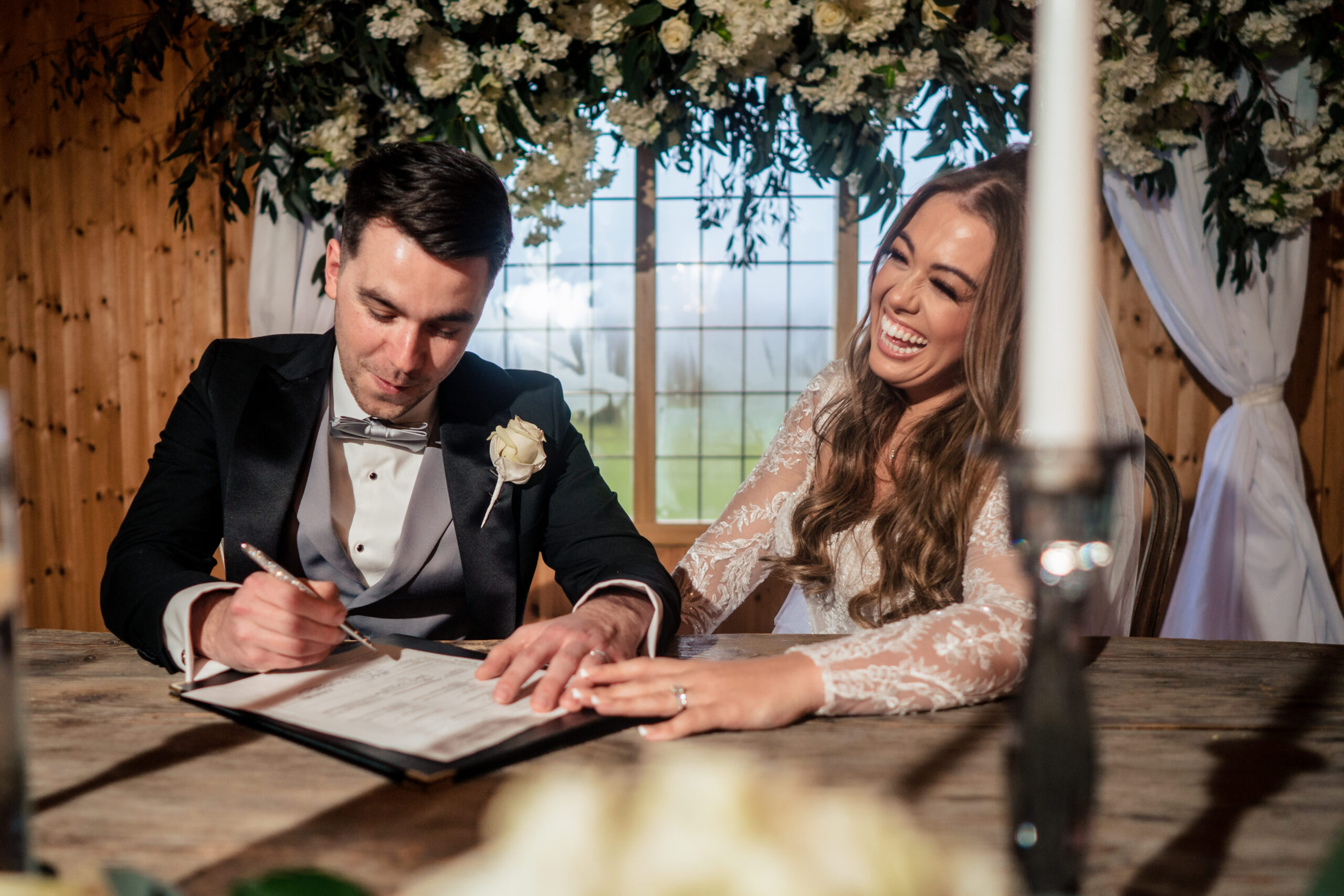 Abbie laughing as Jamie signs the register by candlelight at Merrydale Manor