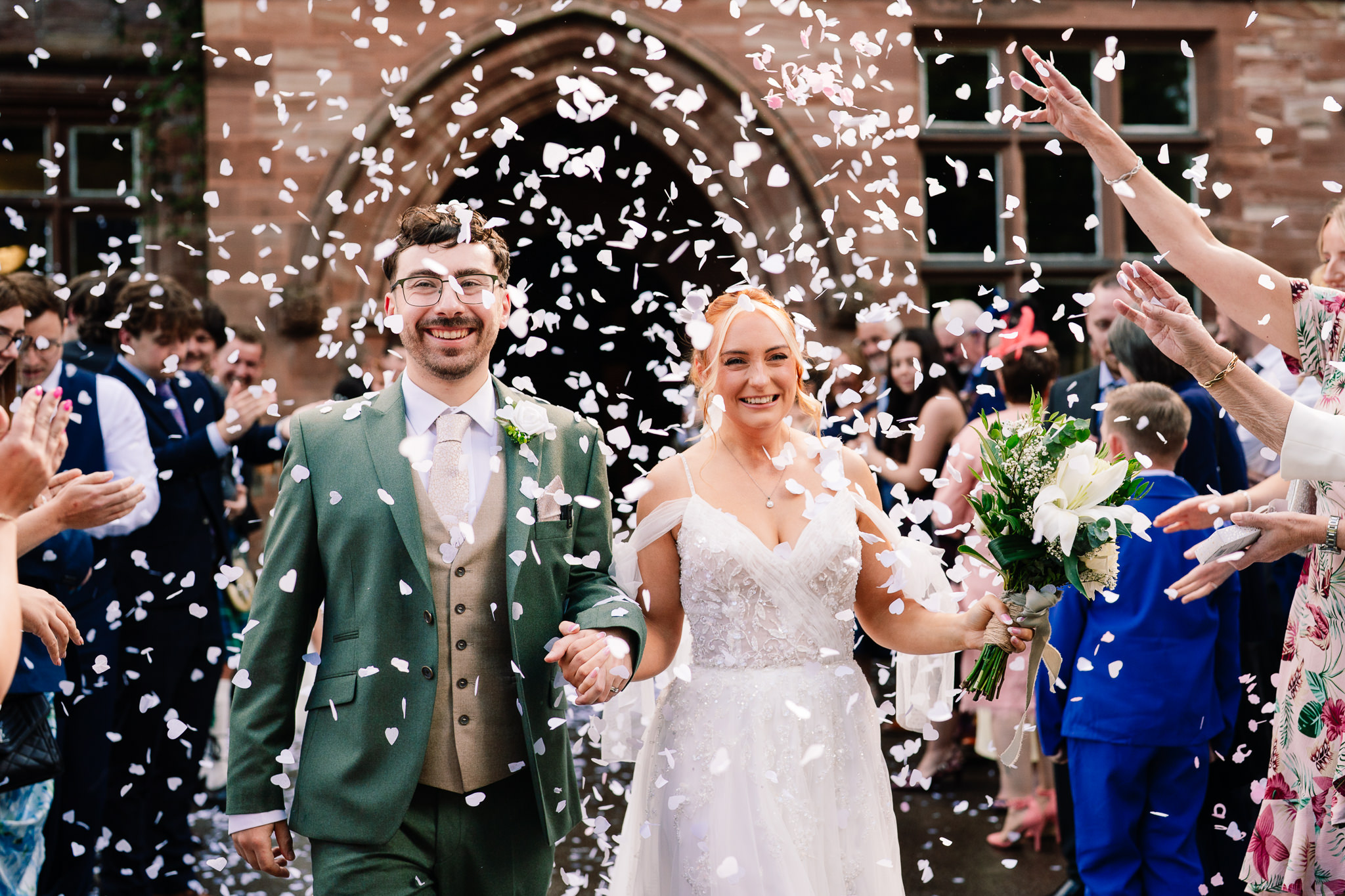 Bride and groom walking through a confetti tunnel with guests cheering either side