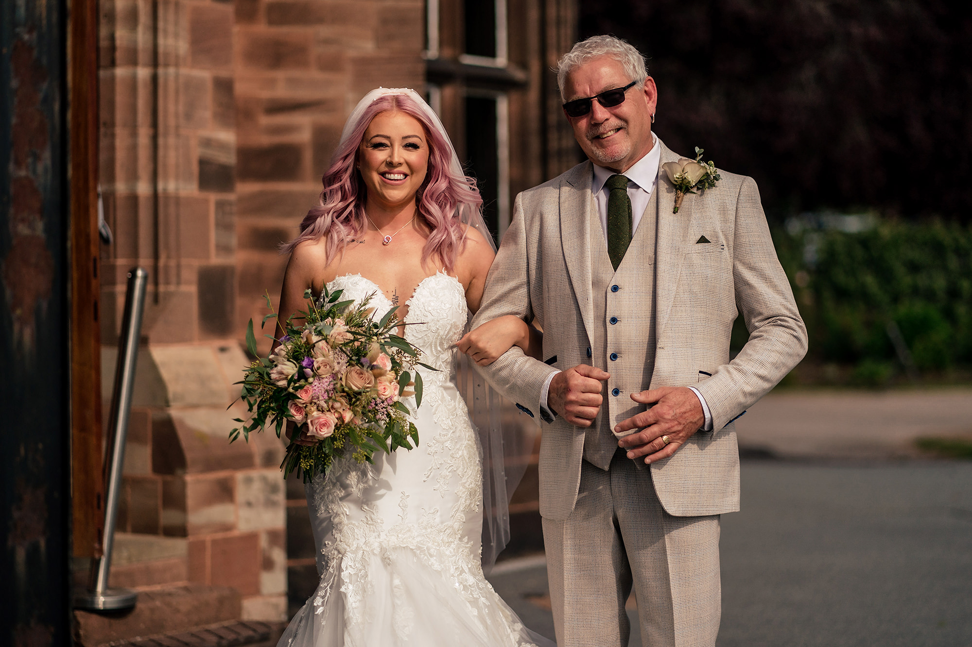 Bride and her dad walking out of the sandstone doorway at Standon Hall ahead of the ceremony