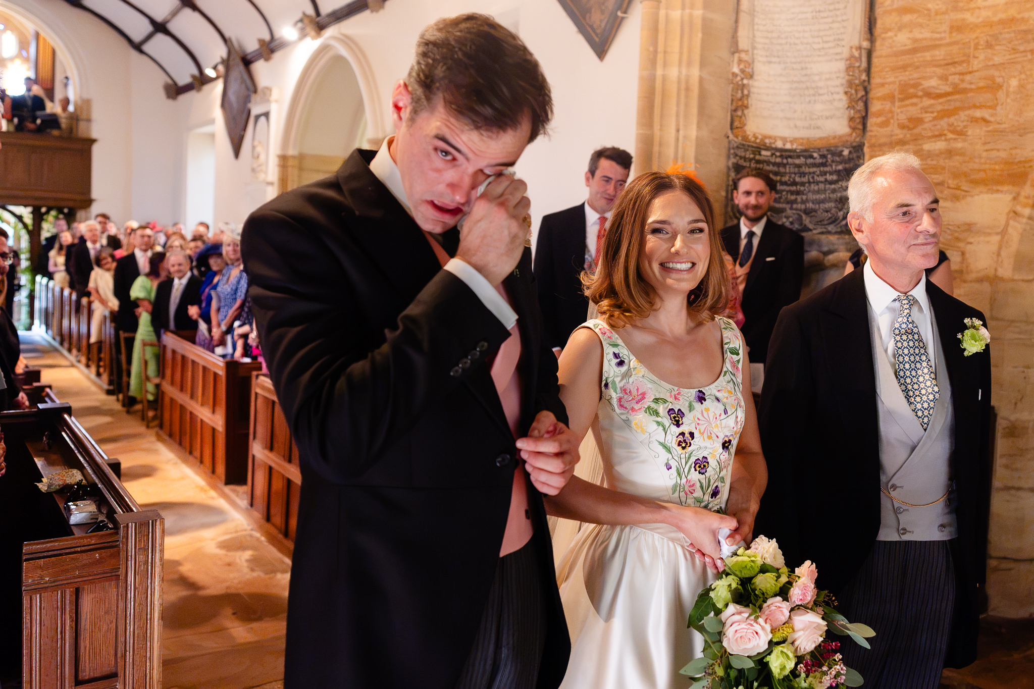 Member of the wedding party wiping away a tear as the bride reaches the front of the church