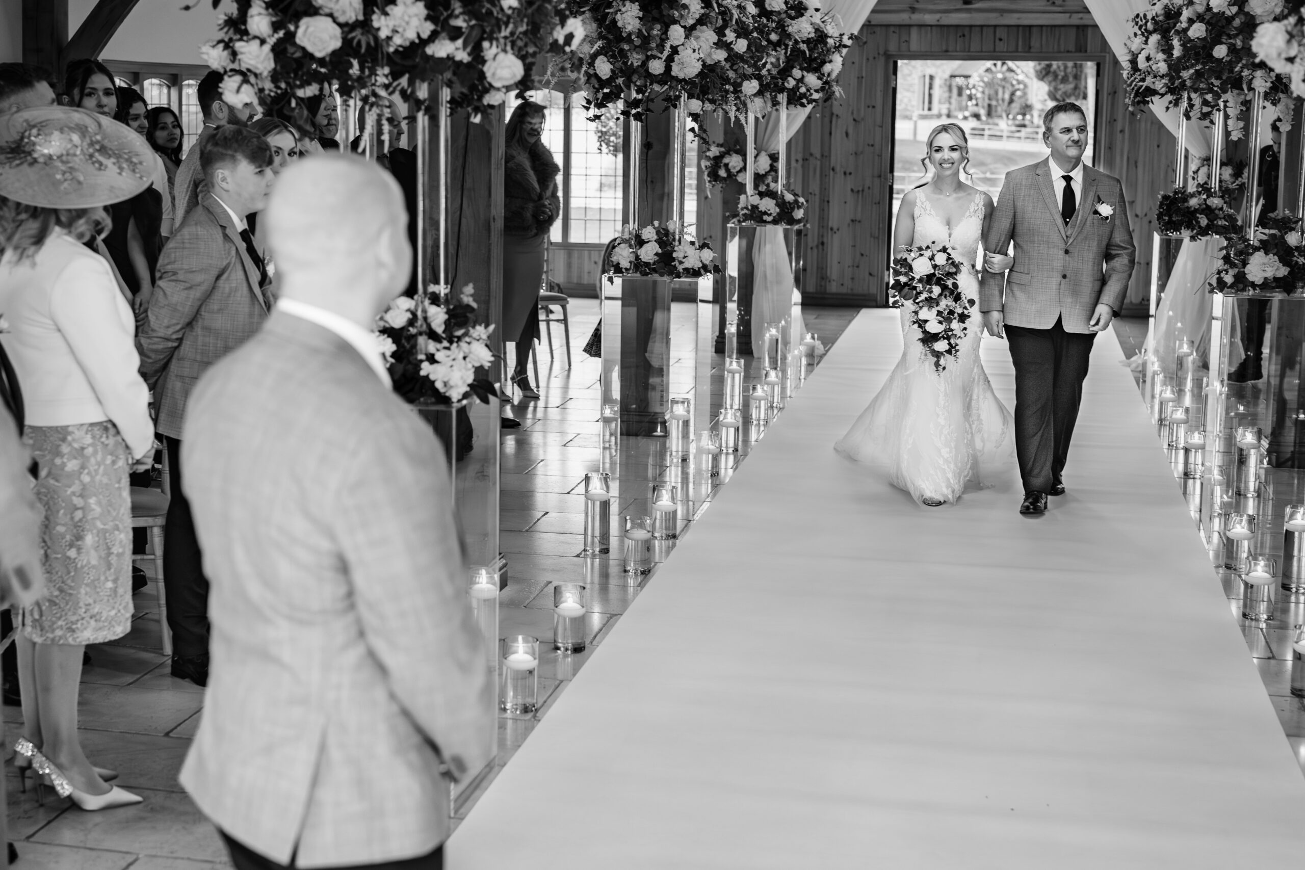 Black and white photo of the bride walking down the candlelit aisle on her dad's arm, Colshaw Hall Ceremony Hall