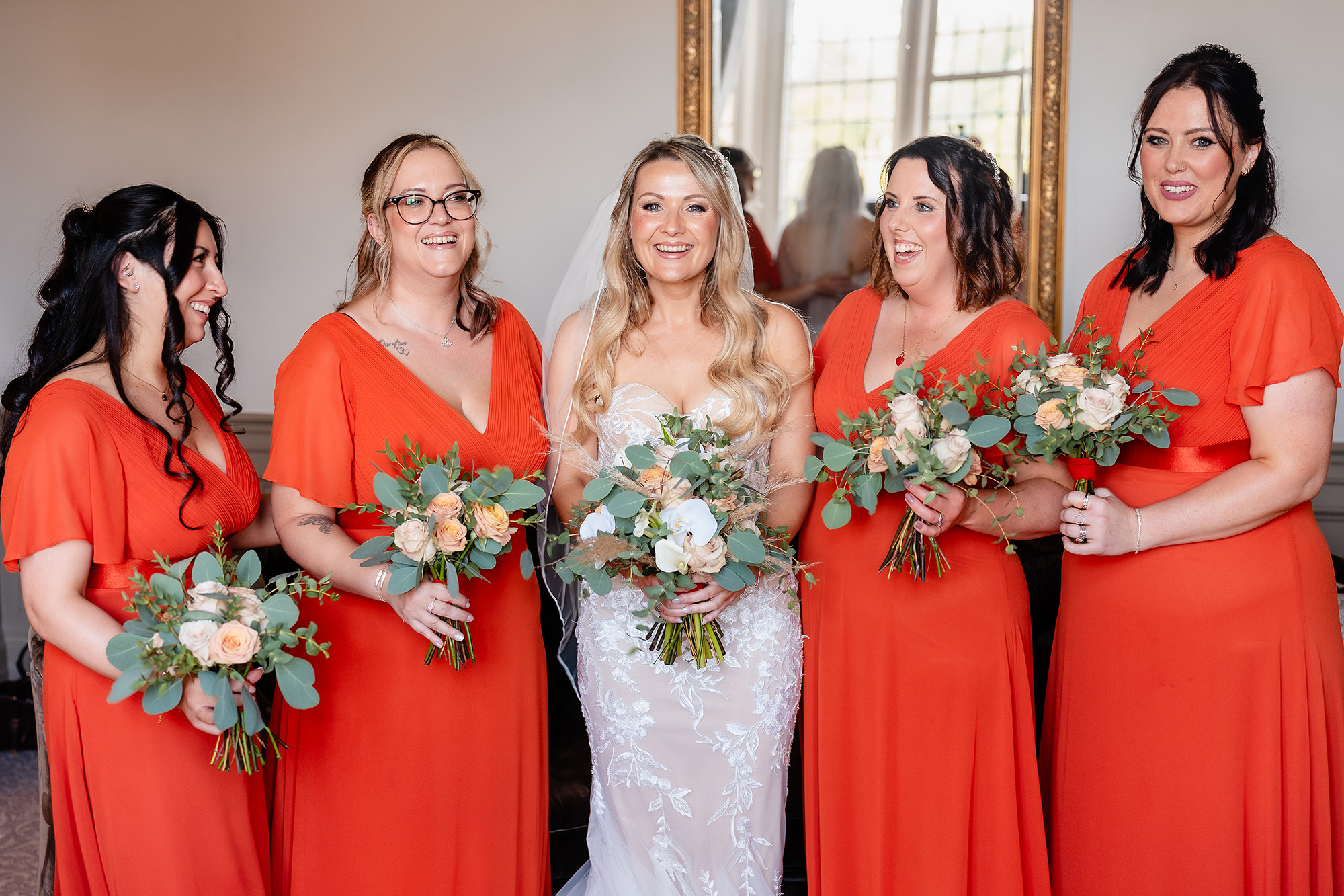 The bride laughing with four bridesmaids in long burnt orange dresses holding peach and cream bouquets, Cheshire wedding photographer