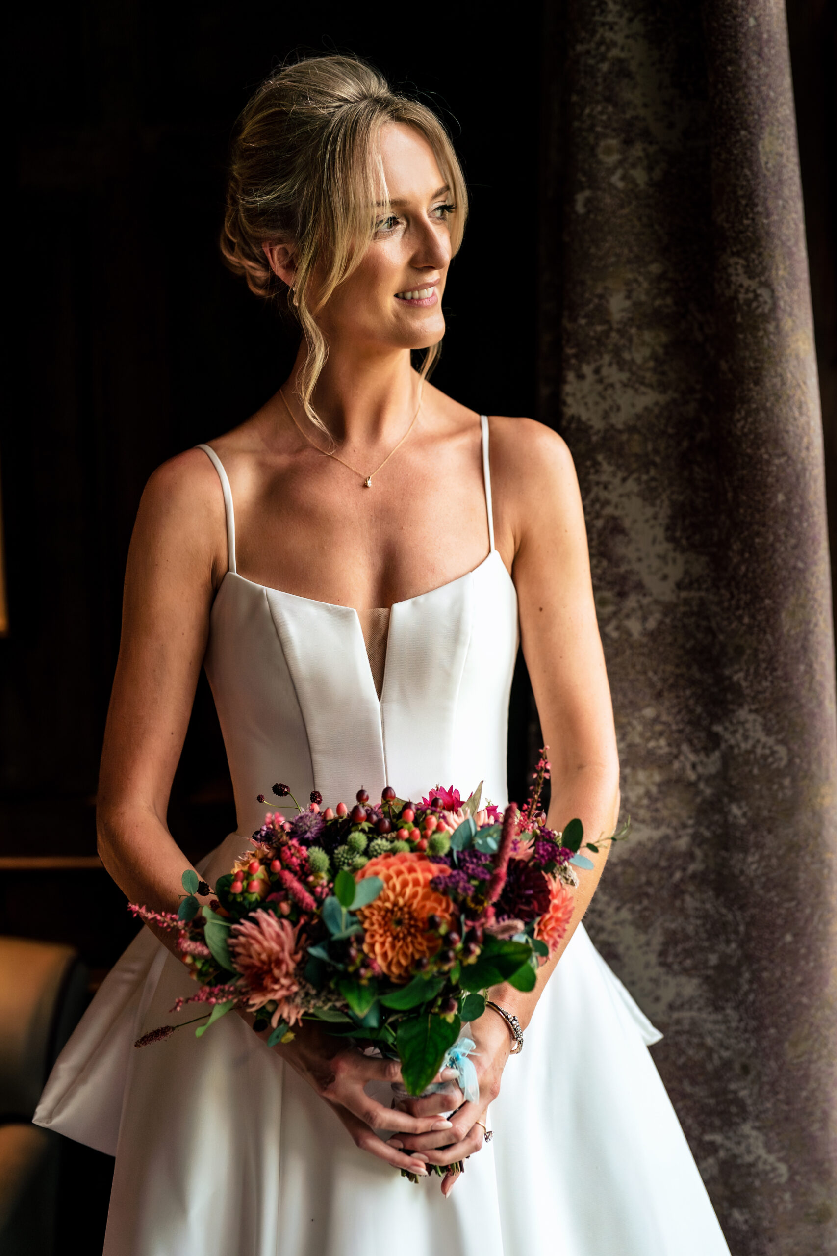 Portrait of the bride holding her dahlia bouquet in window light at Dorfold Hall