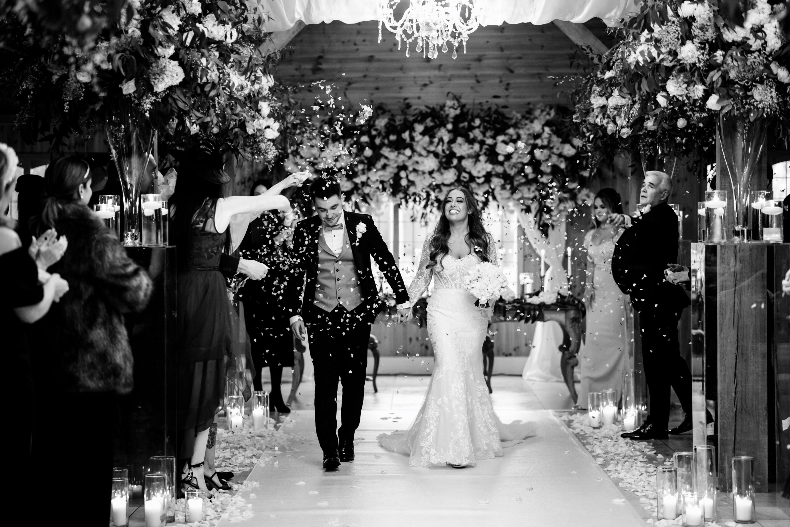 Black and white of guests throwing confetti over Abbie and Jamie in the ceremony room at Merrydale Manor