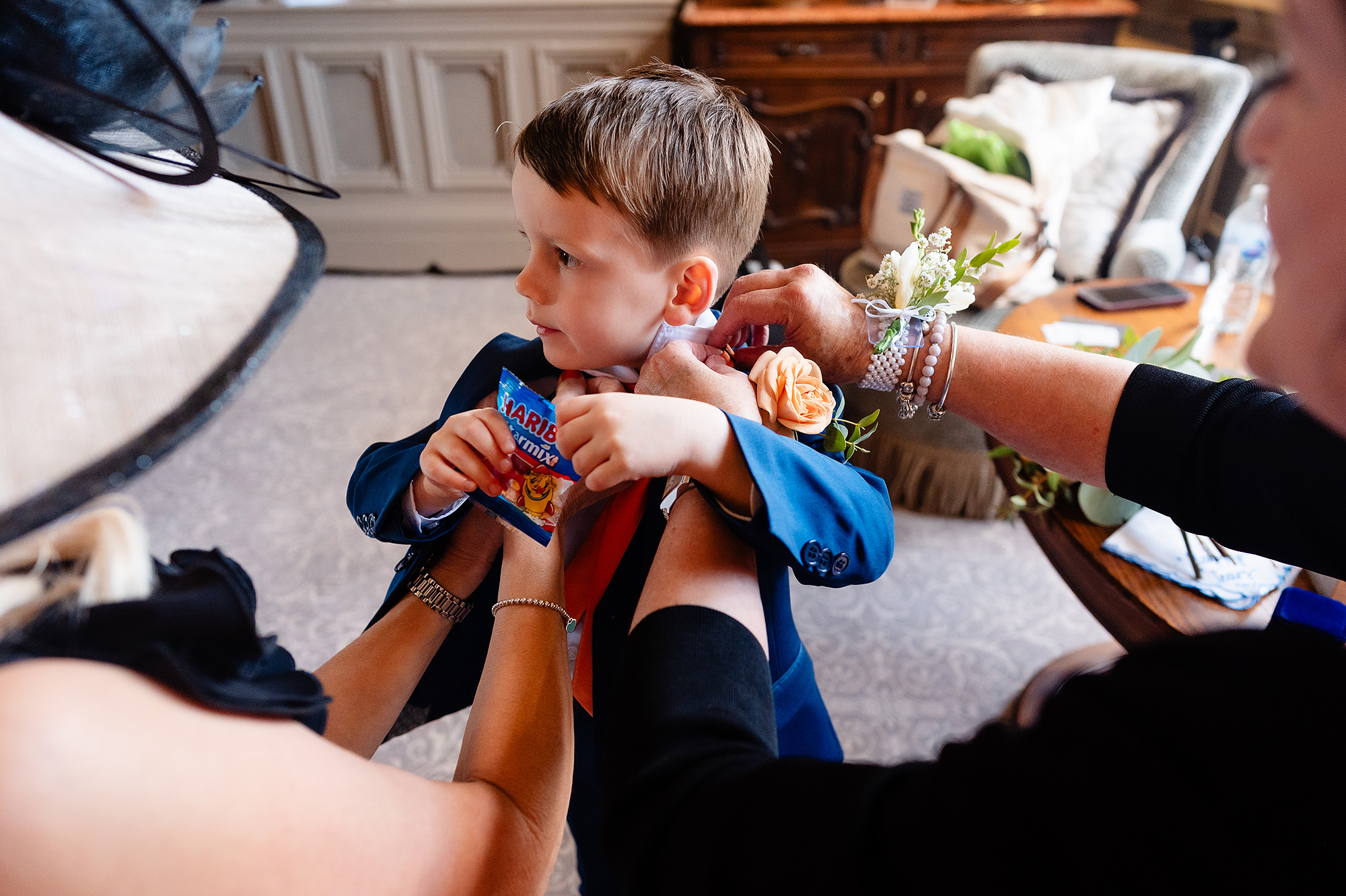 A small boy holding a packet of sweets while a buttonhole is pinned to his navy jacket