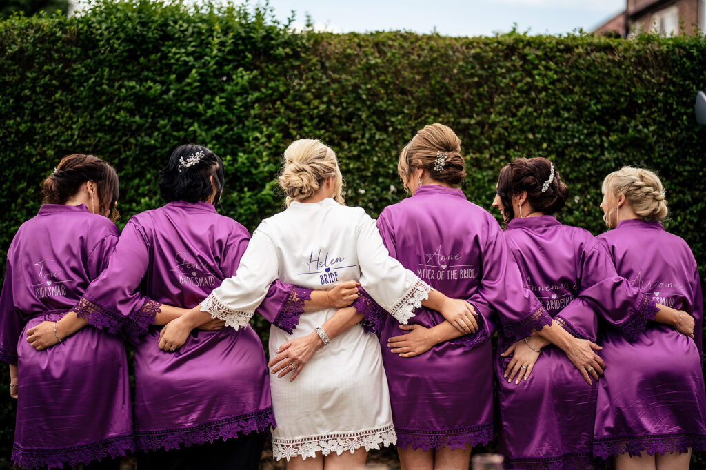Bride and bridal party from behind in matching robes with arms linked, Merrydale Manor wedding photographer