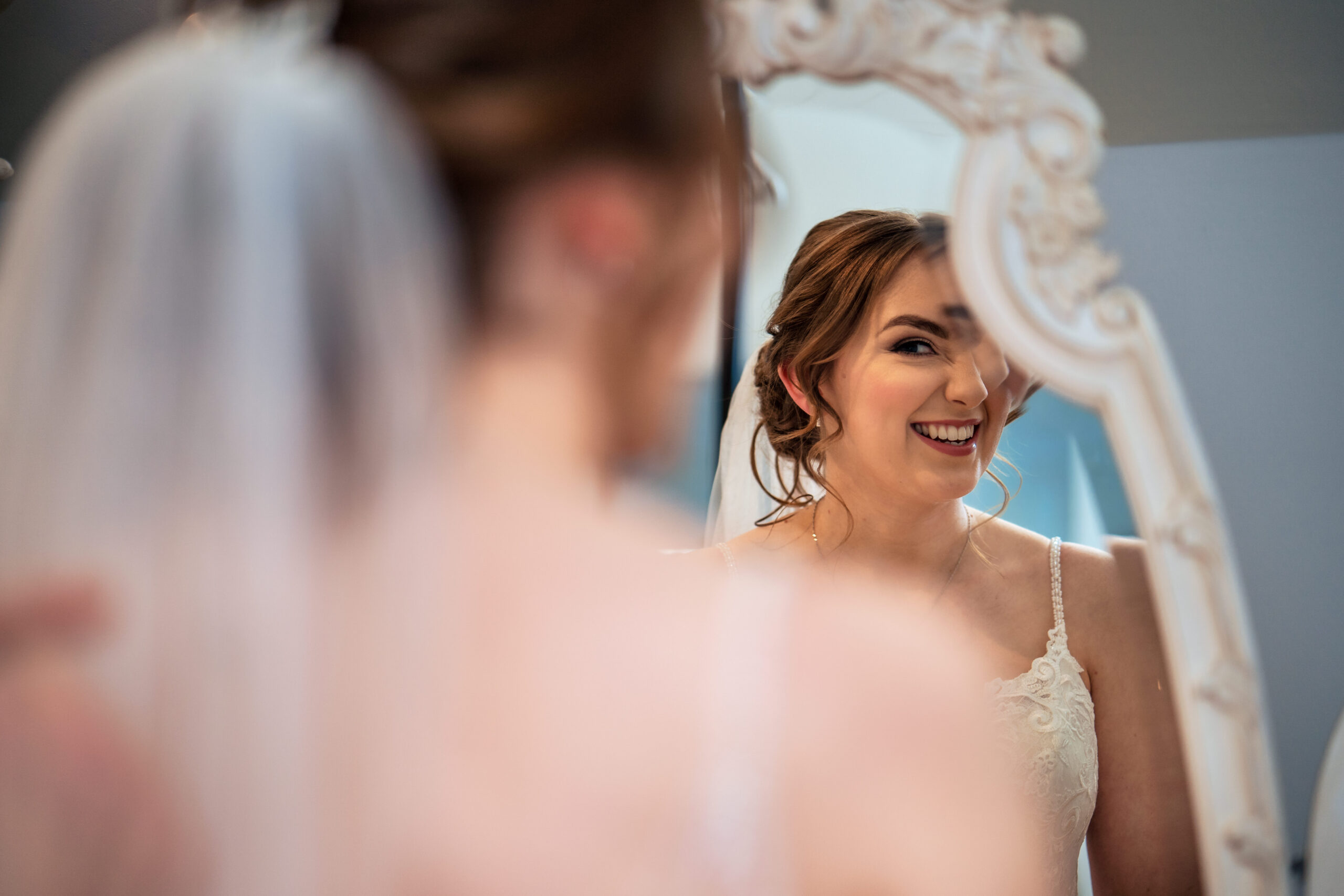 Bethany laughing at her reflection in an ornate white mirror with her veil in