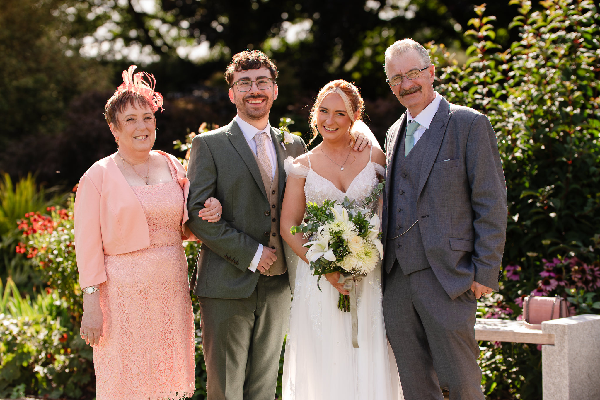 Bride and groom with parents in a family formal photo in the gardens