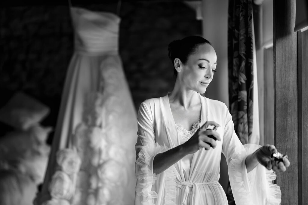 Black and white of Kim in her robe spraying perfume beside her hanging wedding dress, Nottingham wedding photographer
