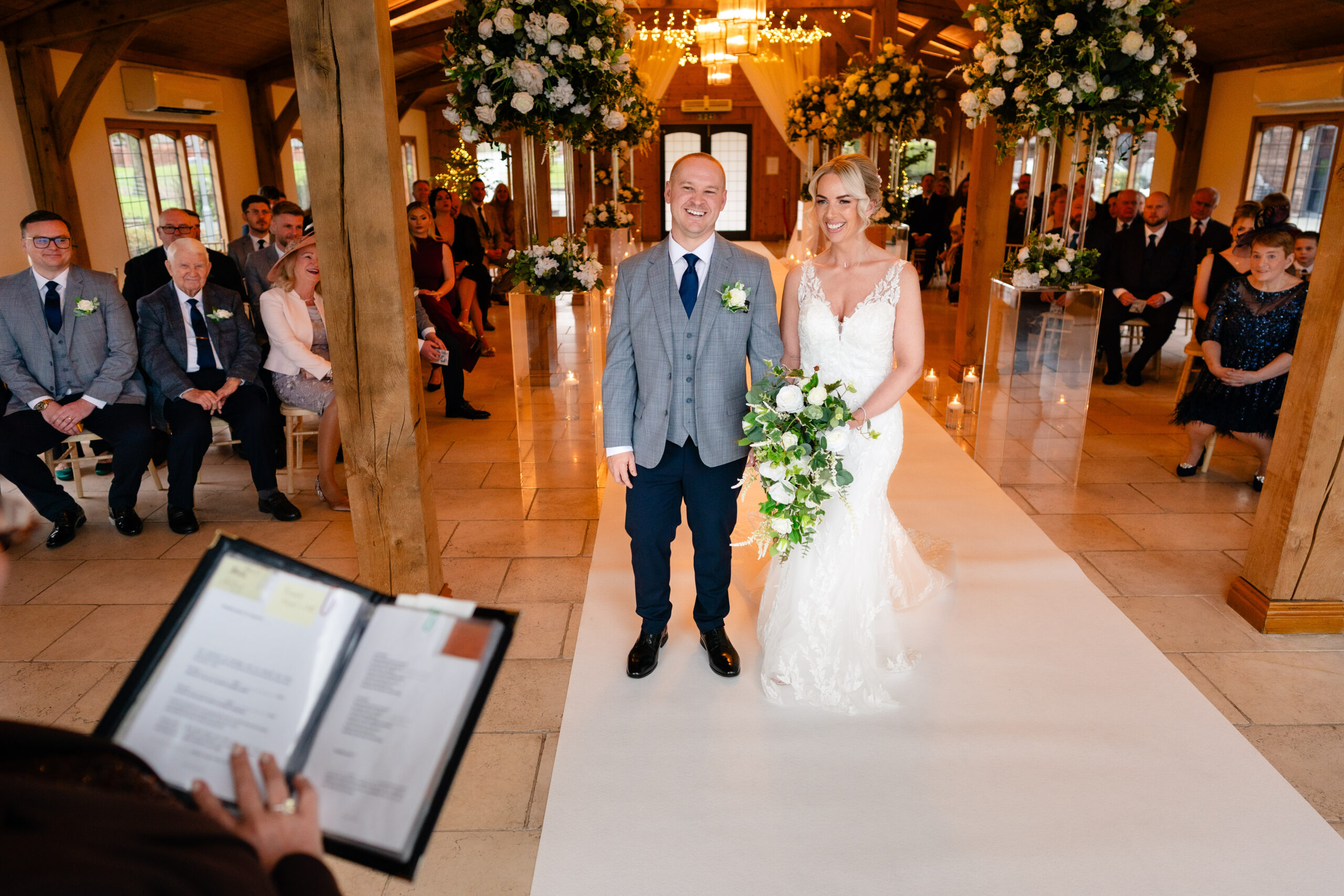 Bride and groom grinning at the top of the aisle as the registrar begins the ceremony, Colshaw Hall Cheshire wedding