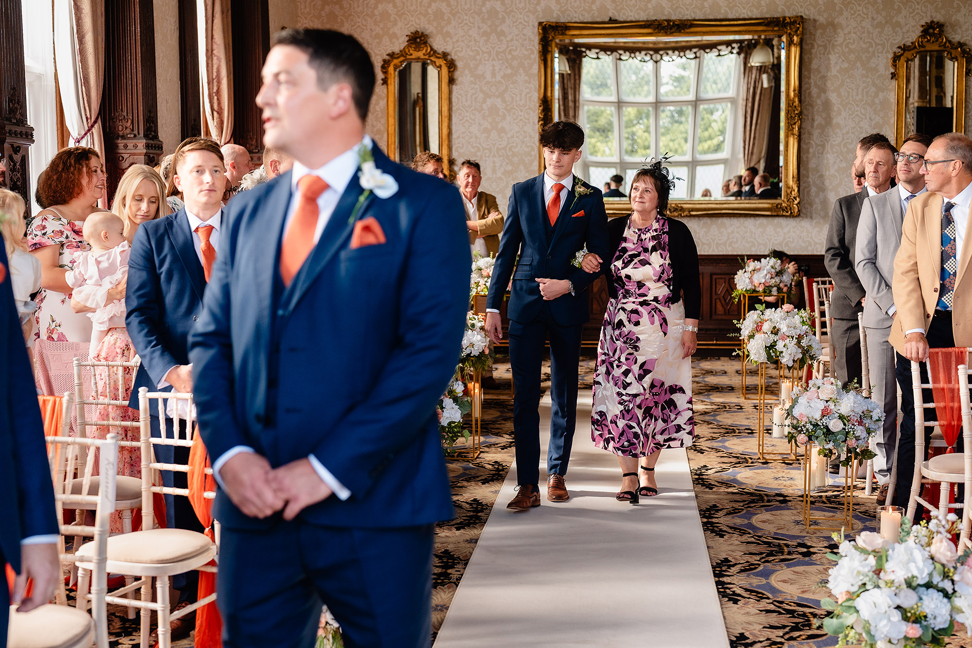 The groom waiting at the top of the aisle in the Drawing Room at Crewe Hall as the processional starts