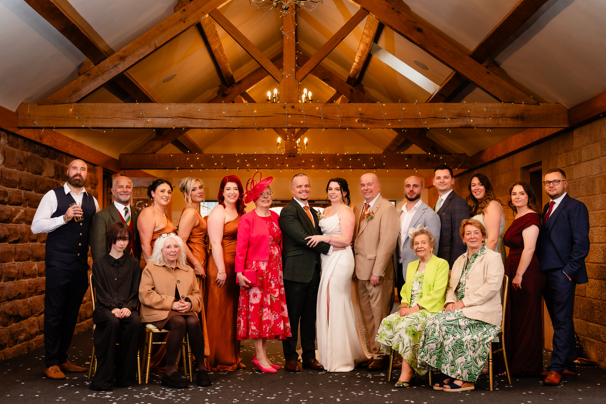 Large family group photo under the vaulted wooden beams and fairy lights of the ceremony barn, Heaton House Farm wedding photographer