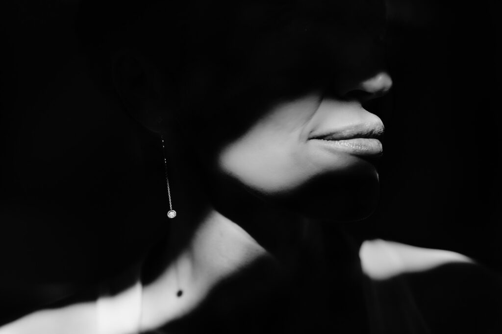 Black and white close up of Kim's lips, neck and drop earring in hard light and deep shadow, Swancar Farm wedding photographer