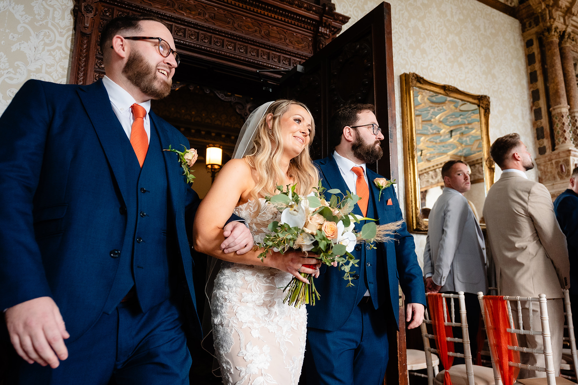 The bride arriving at the front of the ceremony arm in arm with her two brothers, all three grinning