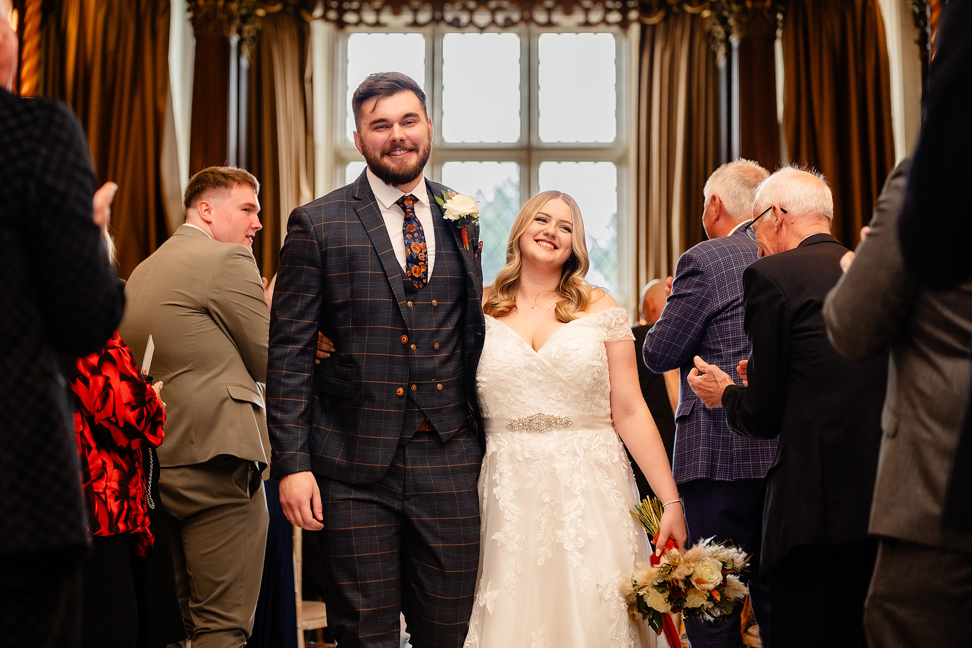 Annie and Tom walking hand in hand through cheering guests at Crewe Hall, Cheshire wedding photographer