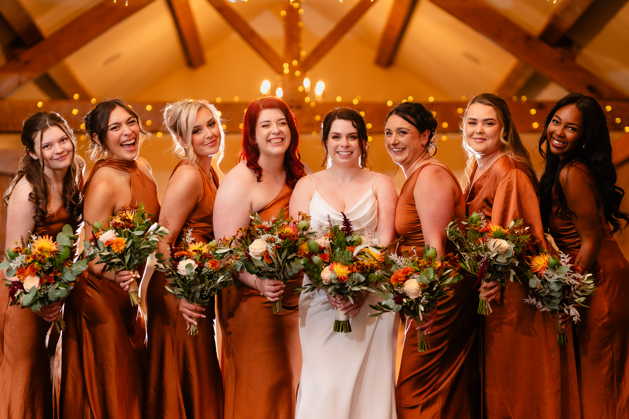 Bride with her bridesmaids in burnt orange satin dresses holding autumn bouquets, Heaton House Farm Cheshire wedding photographer