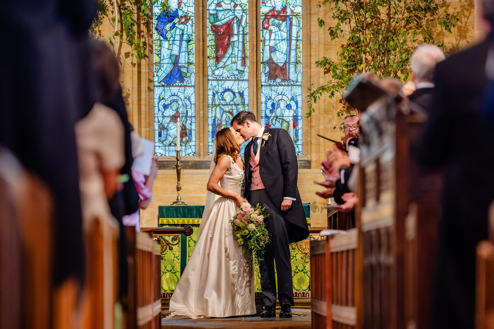Bride and groom share their first kiss as a married couple, framed by the church pews