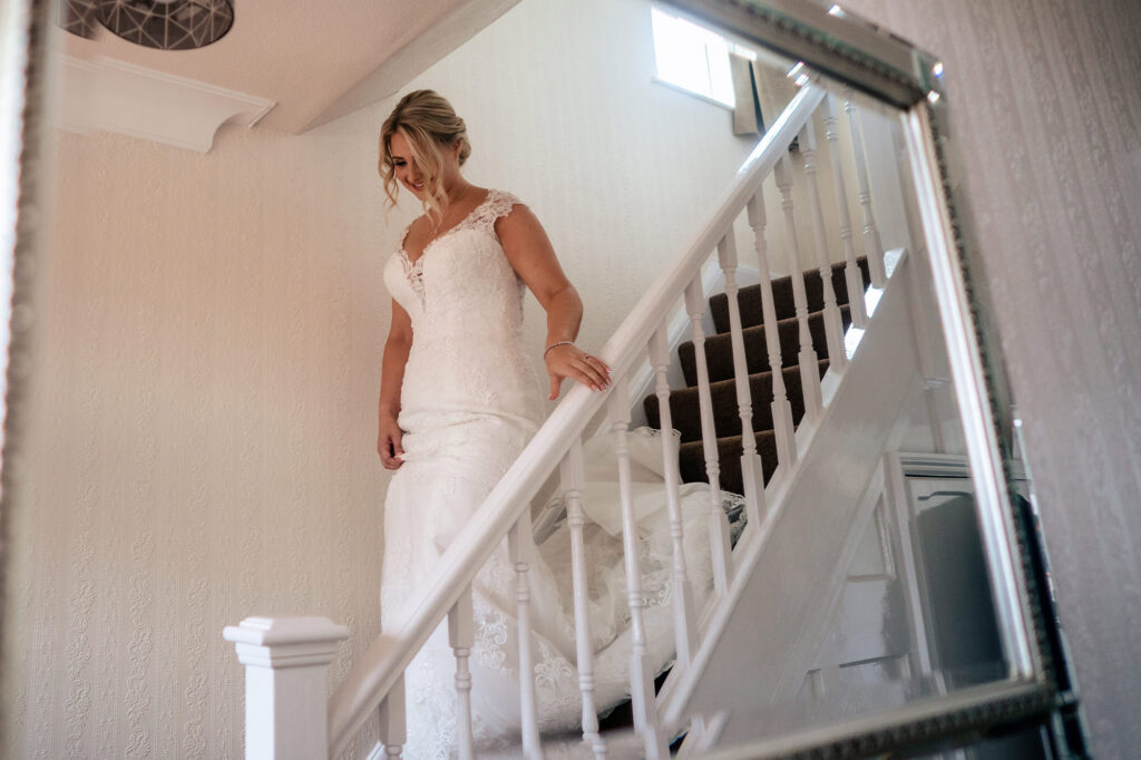 Bride walking down the stairs in her lace wedding dress, reflected in a mirror, Merrydale Manor wedding photographer