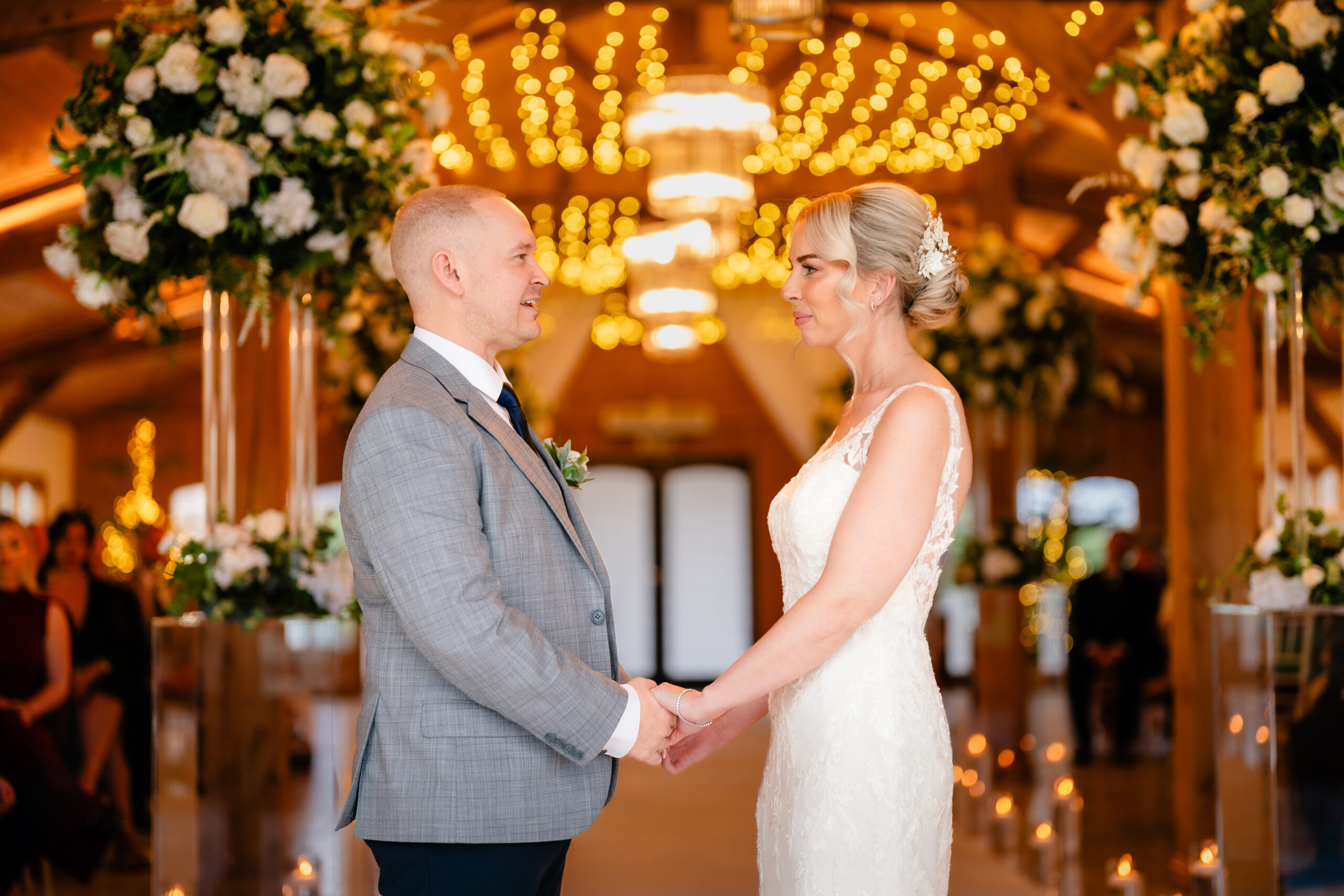 Bride and groom holding hands and looking at each other under the fairy lights and chandeliers of the Ceremony Hall, Colshaw Hall wedding