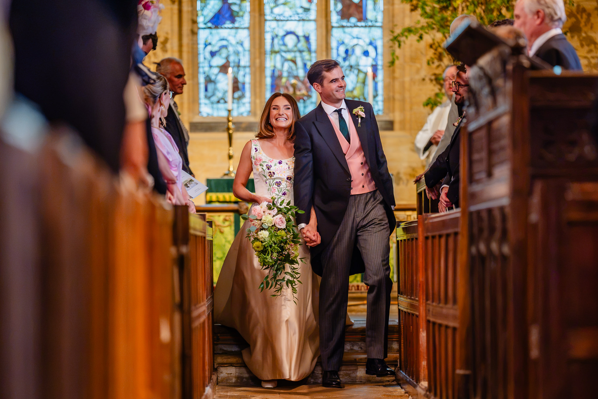 Newly married couple walking back up the aisle as their guests cheer