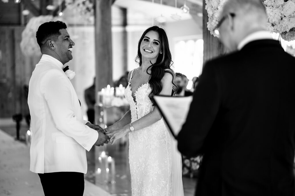 Black and white photo of Gemma and Tyrone laughing as they hold hands during their vows at Merrydale Manor