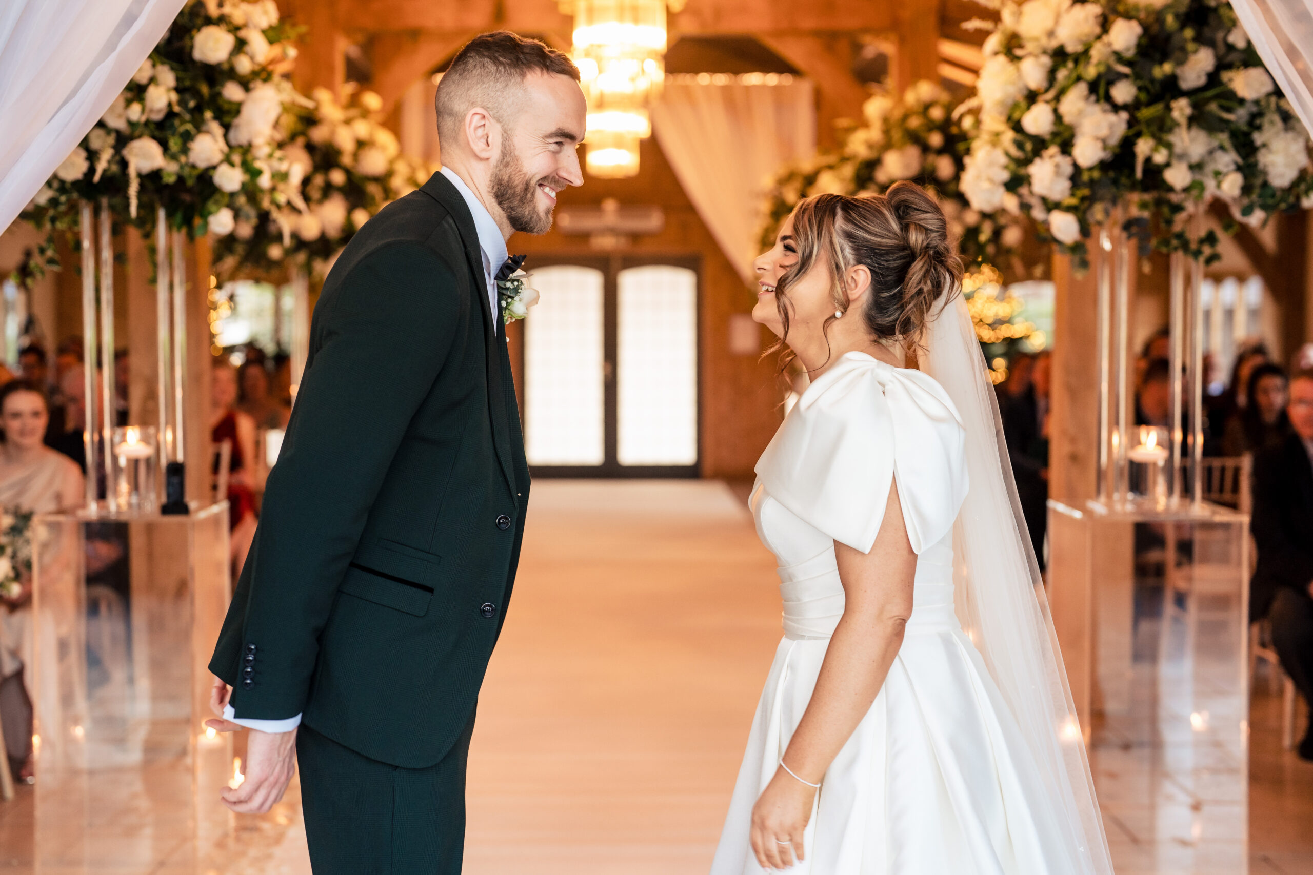 Georgia and Joe sharing a look at the front of the ceremony room, floral arch behind them