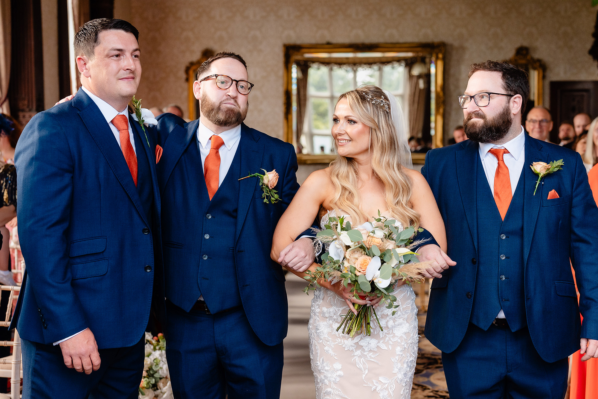 The bride at the front of the Drawing Room with three men in navy suits, her bouquet held in front of her