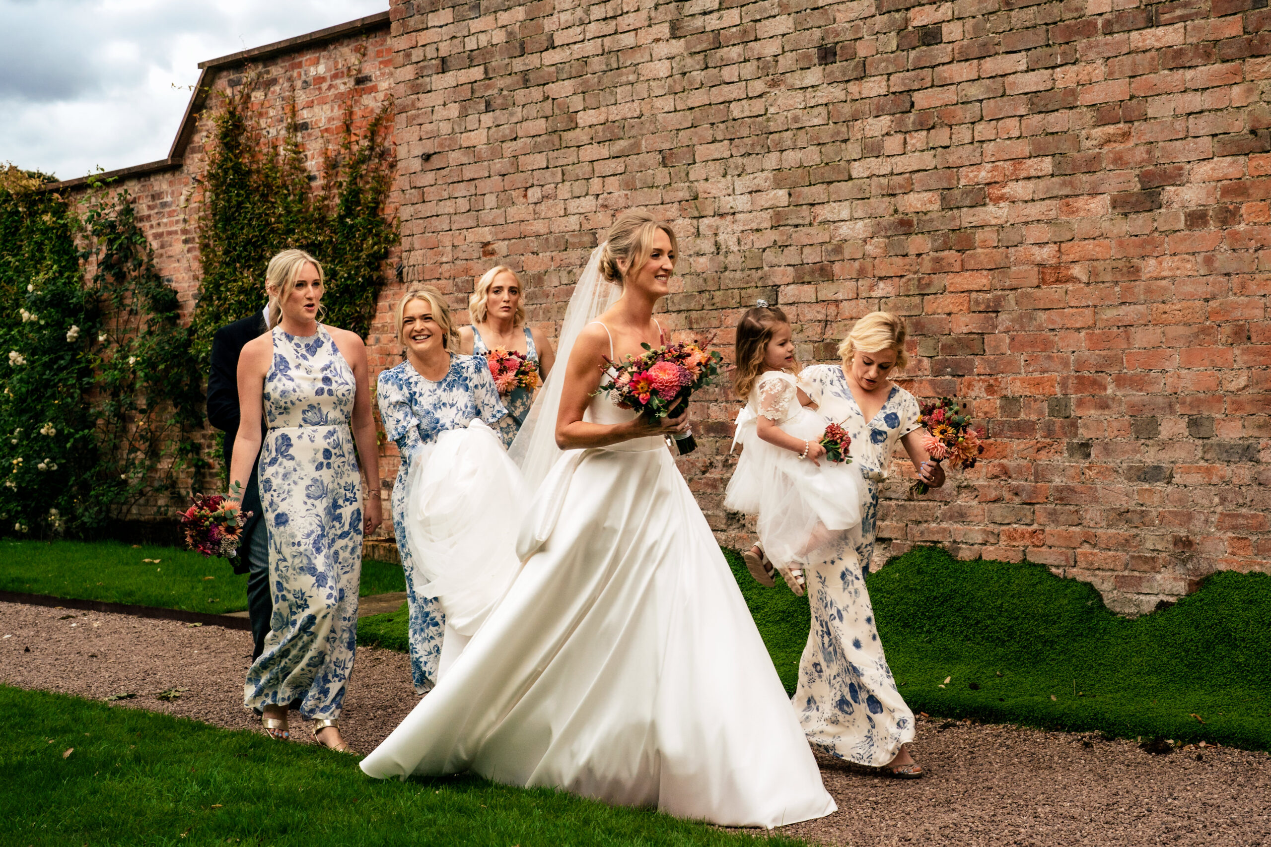 Bride and bridesmaids walking along a brick garden wall on their way to the Coach House ceremony at Dorfold Hall