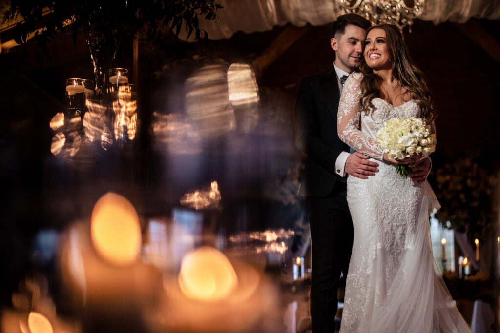 Jamie with his arm around Abbie behind the warm blur of candle flames, Cheshire wedding photographer