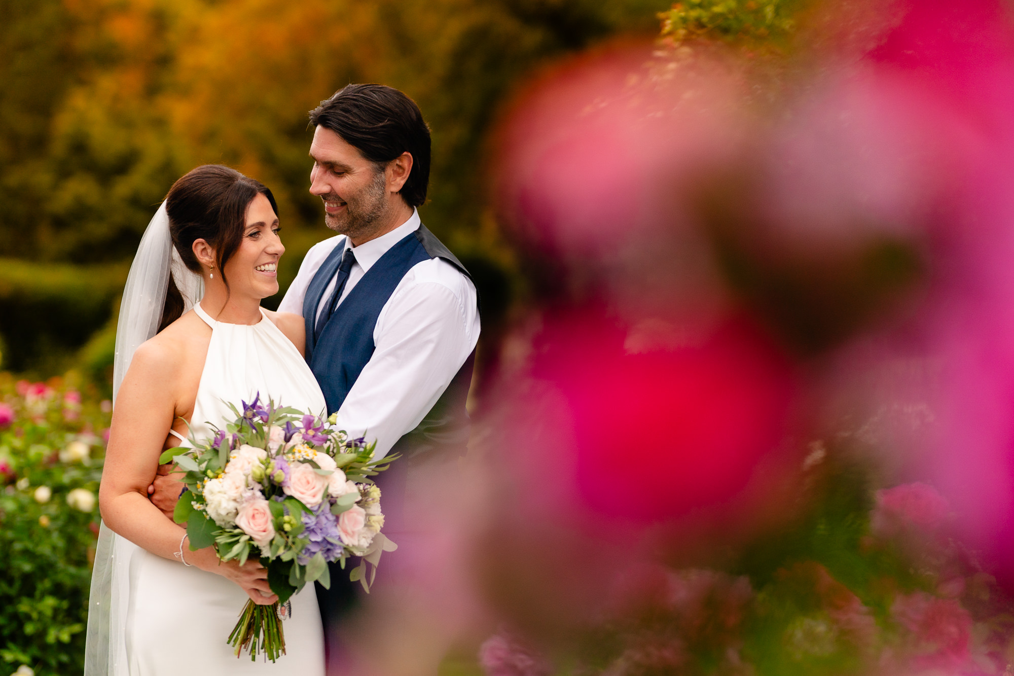 Bride and groom embracing in golden evening light surrounded by pink flowers, Salt House Staffordshire wedding photographer