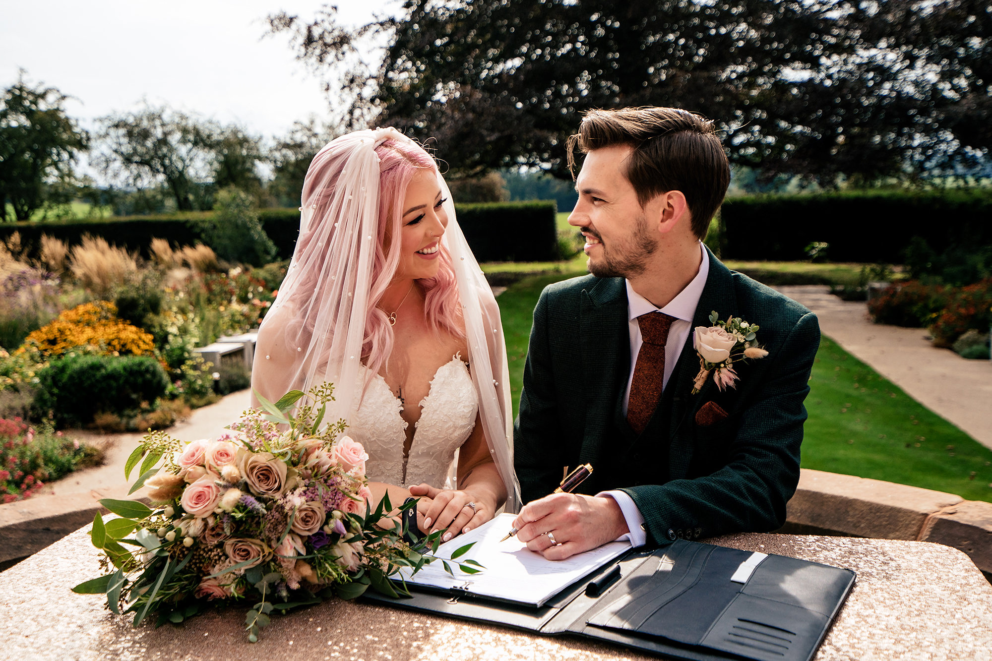 Bride and groom signing the register together in the gardens at Standon Hall