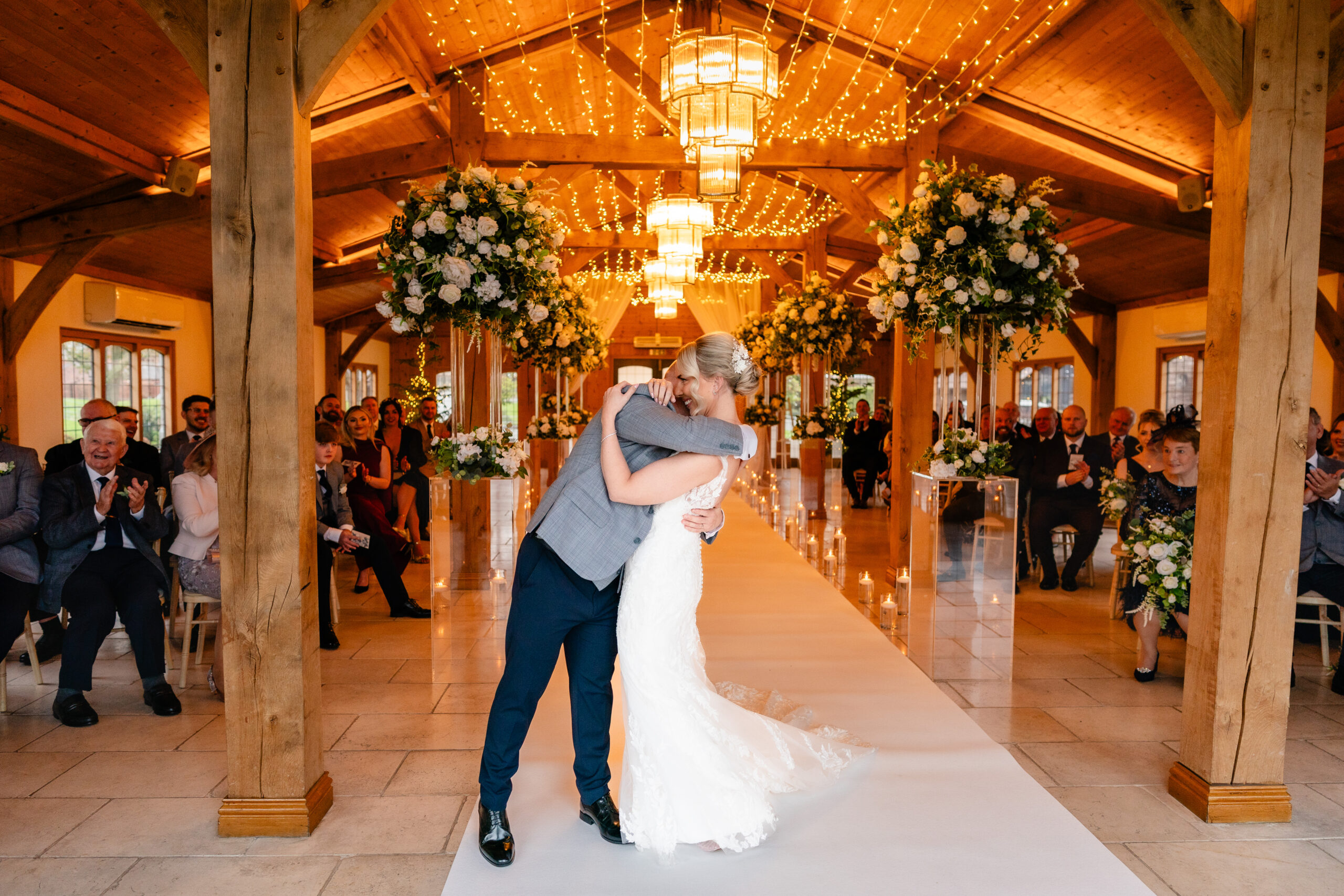 Newly married couple wrapped around each other in the aisle as their guests applaud, Colshaw Hall Ceremony Hall