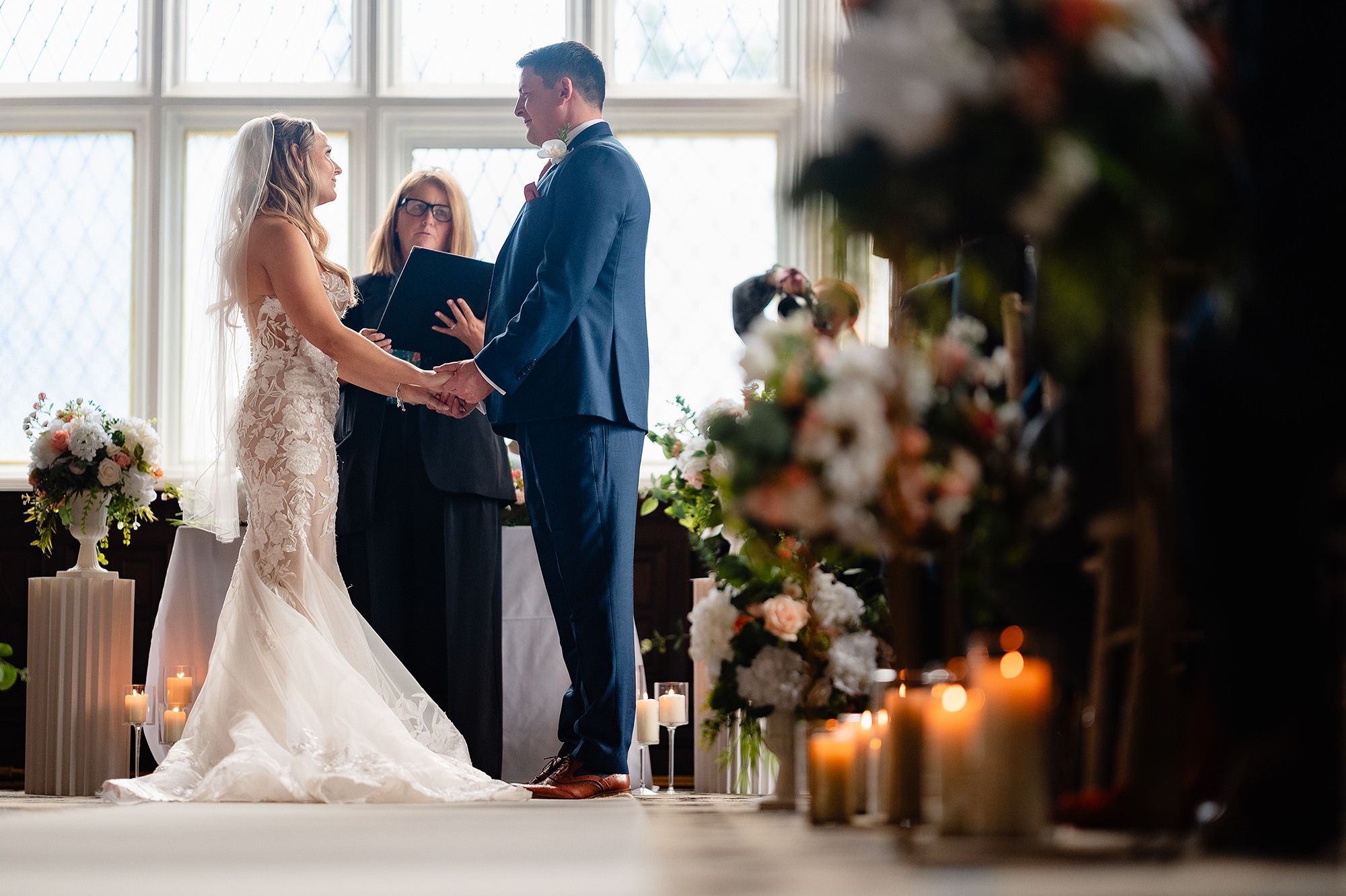 Bride and groom holding hands during their ceremony beside a floral display and a row of lit pillar candles