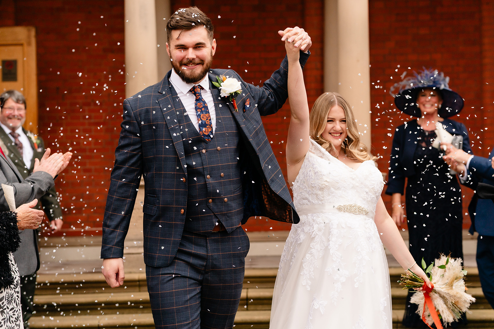 Annie and Tom holding hands up as they walk down the steps through confetti, Crewe Hall wedding photographer