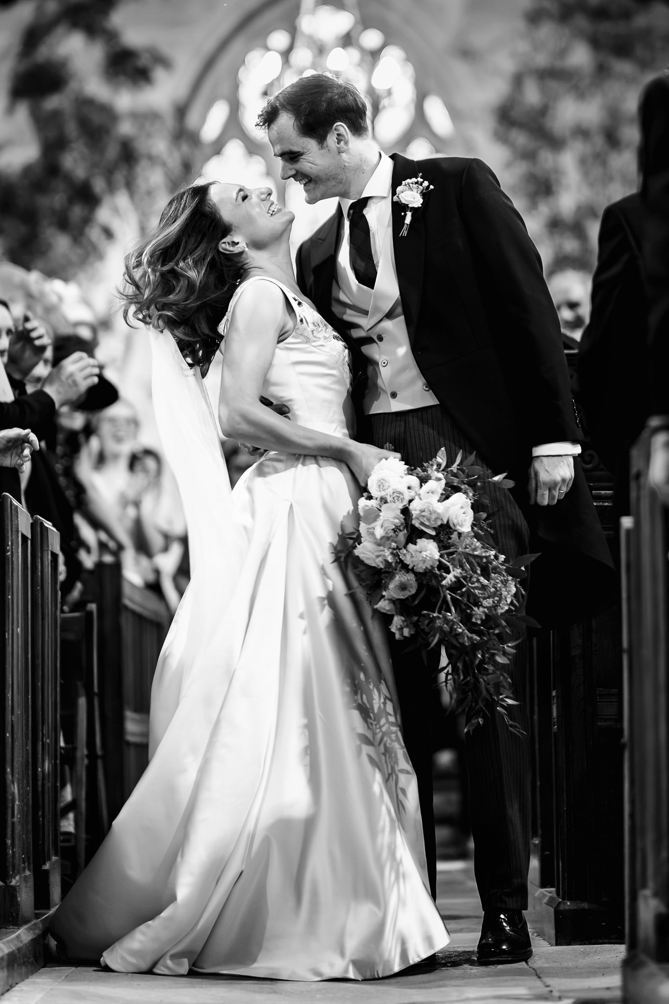 Black and white photograph of the groom dipping his bride for a kiss as they leave the church