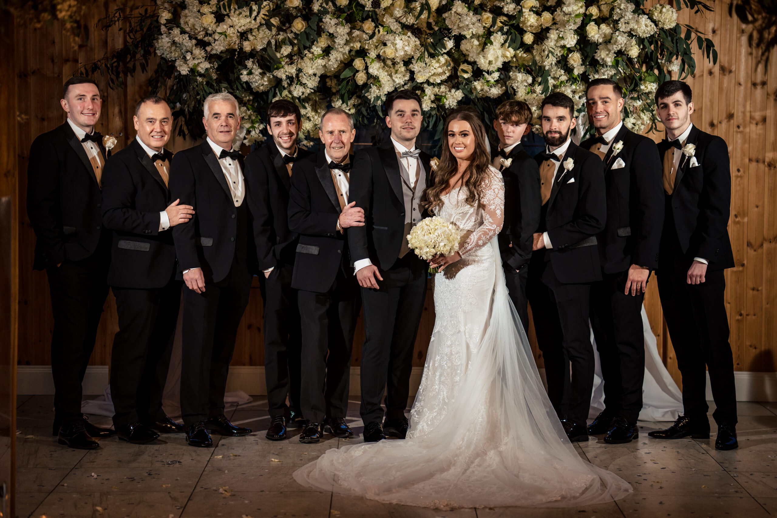 Abbie and Jamie with the men of the wedding party in black tie under the floral wall at Merrydale Manor