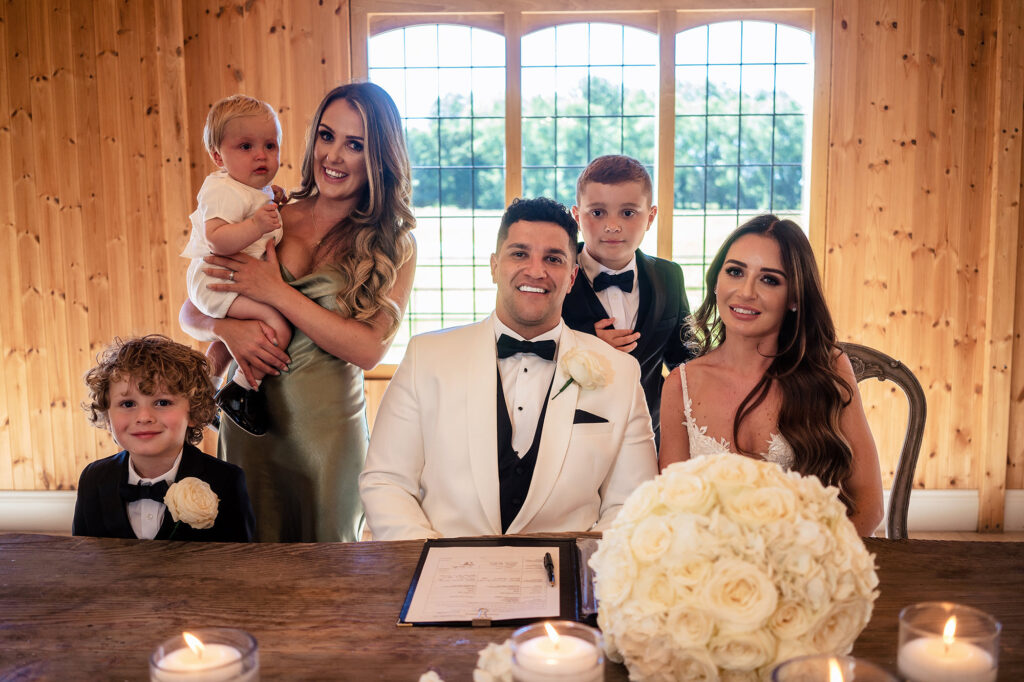 Gemma and Tyrone signing the register with the page boys and a bridesmaid holding a baby at Merrydale Manor