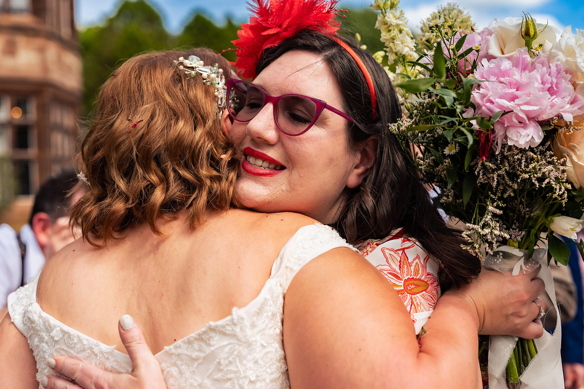 Bride hugging a friend wearing a bold red headpiece just after the ceremony at Salt House