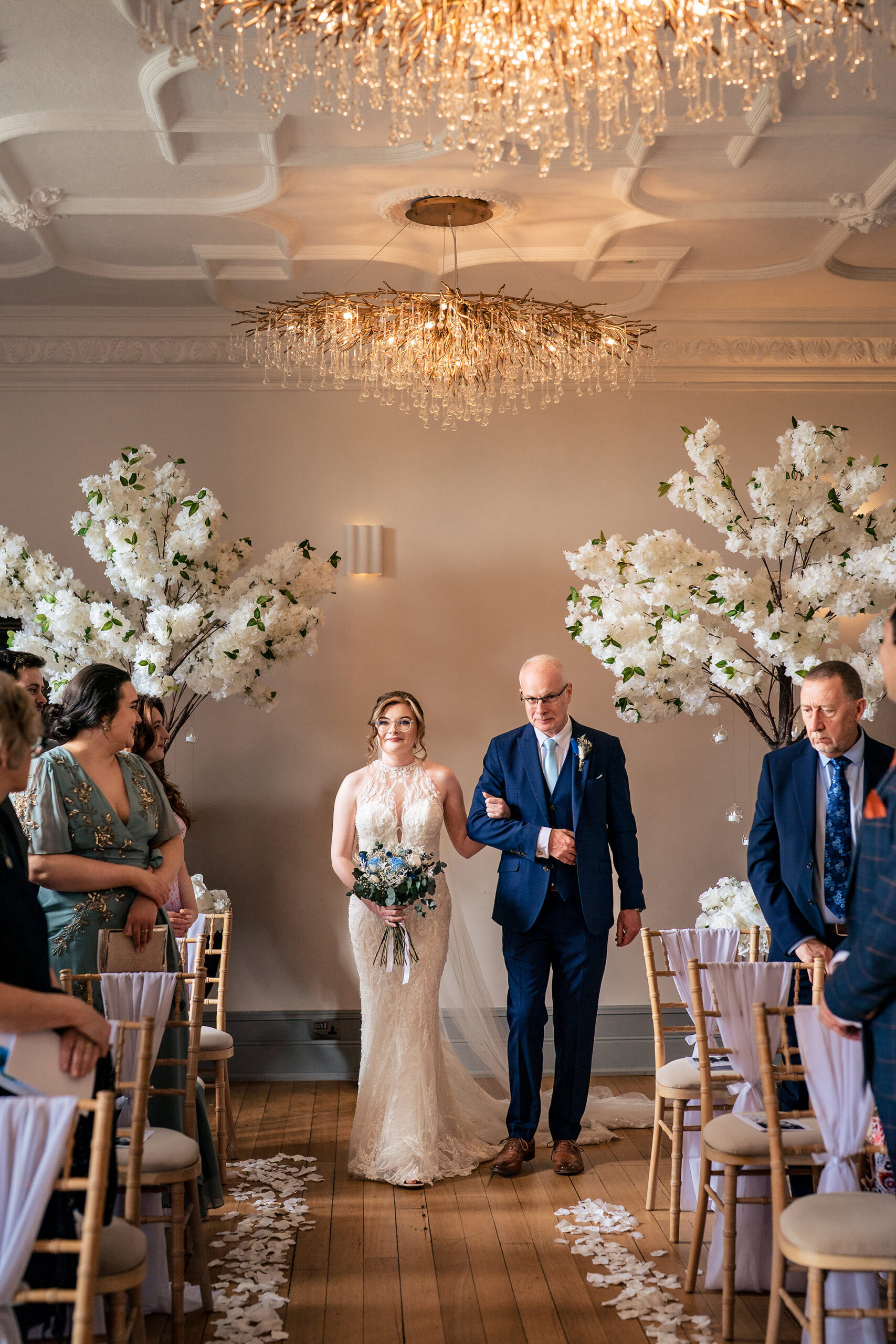 Wide shot of the bride and her dad walking down the aisle beneath the cherry blossom arch at Salt House, Staffordshire wedding photographer