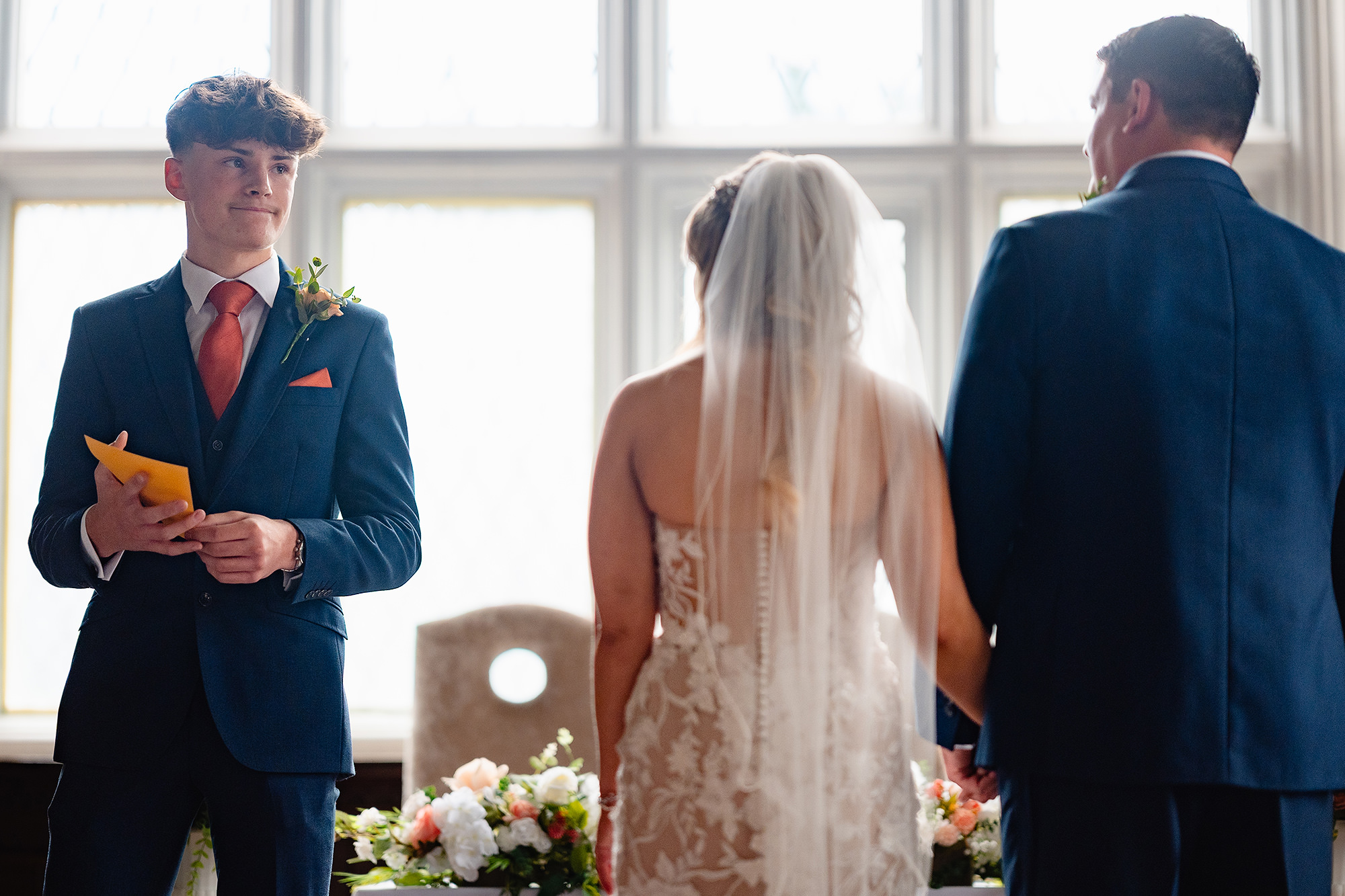 Zach reading from a yellow card during the ceremony while Lauren and Dan hold hands in front of him
