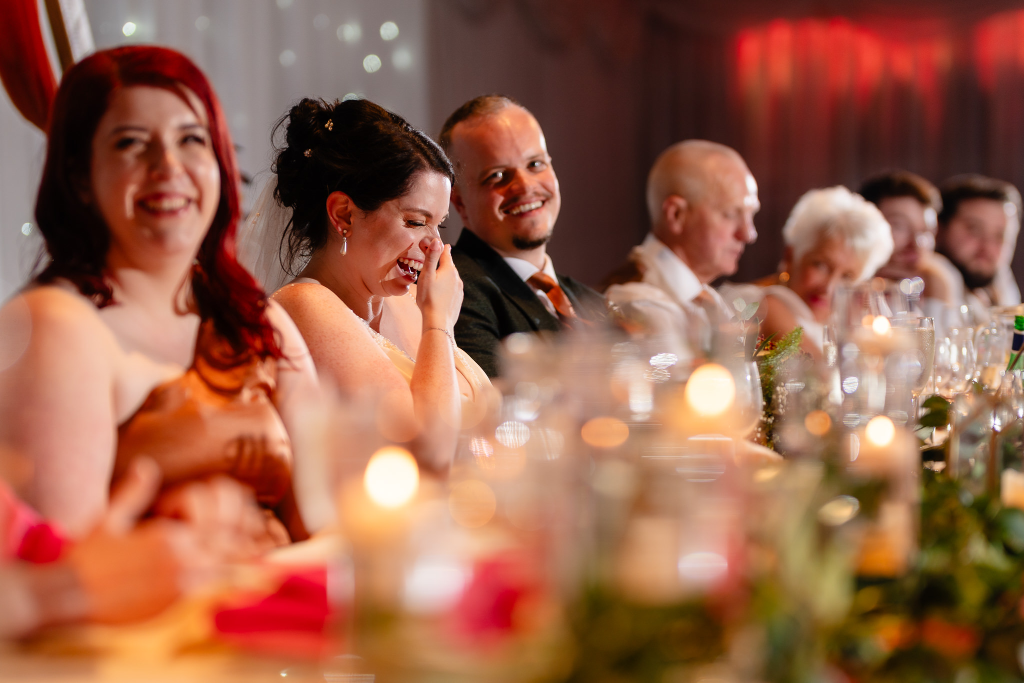 Bride laughing behind her hand during the speeches at the candlelit top table, Heaton House Farm Cheshire wedding photographer