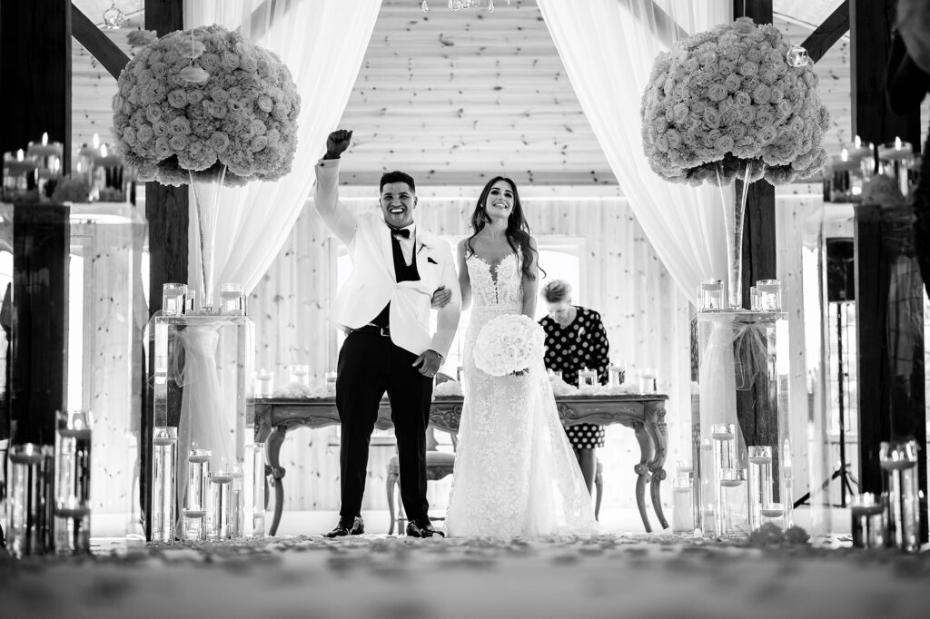Black and white photo of Tyrone punching the air as he and Gemma walk back up the aisle as newlyweds, Merrydale Manor