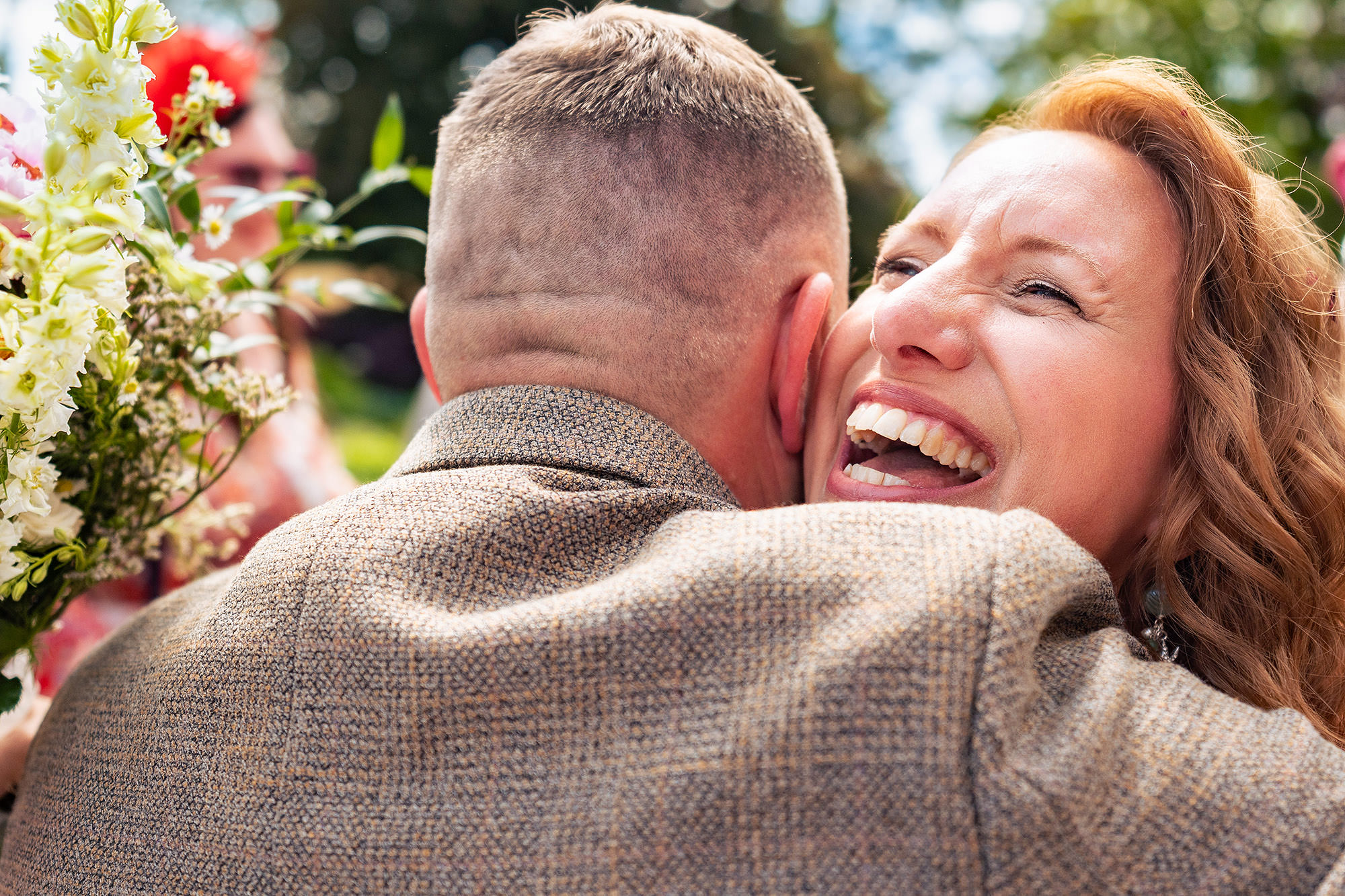Groom laughing while hugging a guest in the gardens after his wedding ceremony