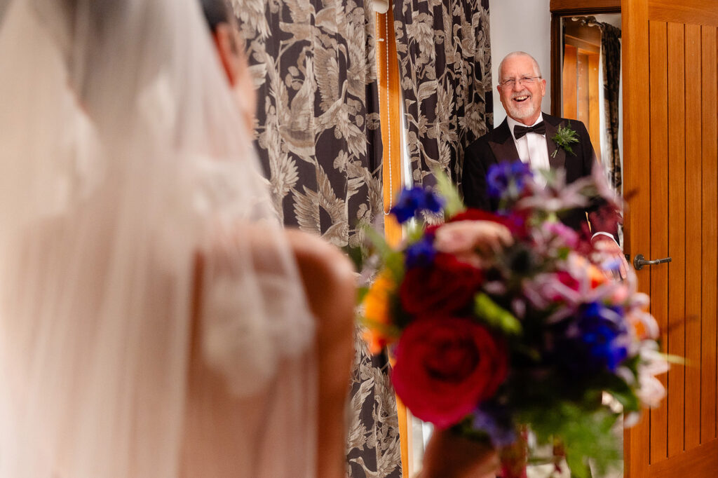 Kim's dad in black tie grinning as he sees her in her dress, bouquet in the foreground, Nottingham wedding photographer