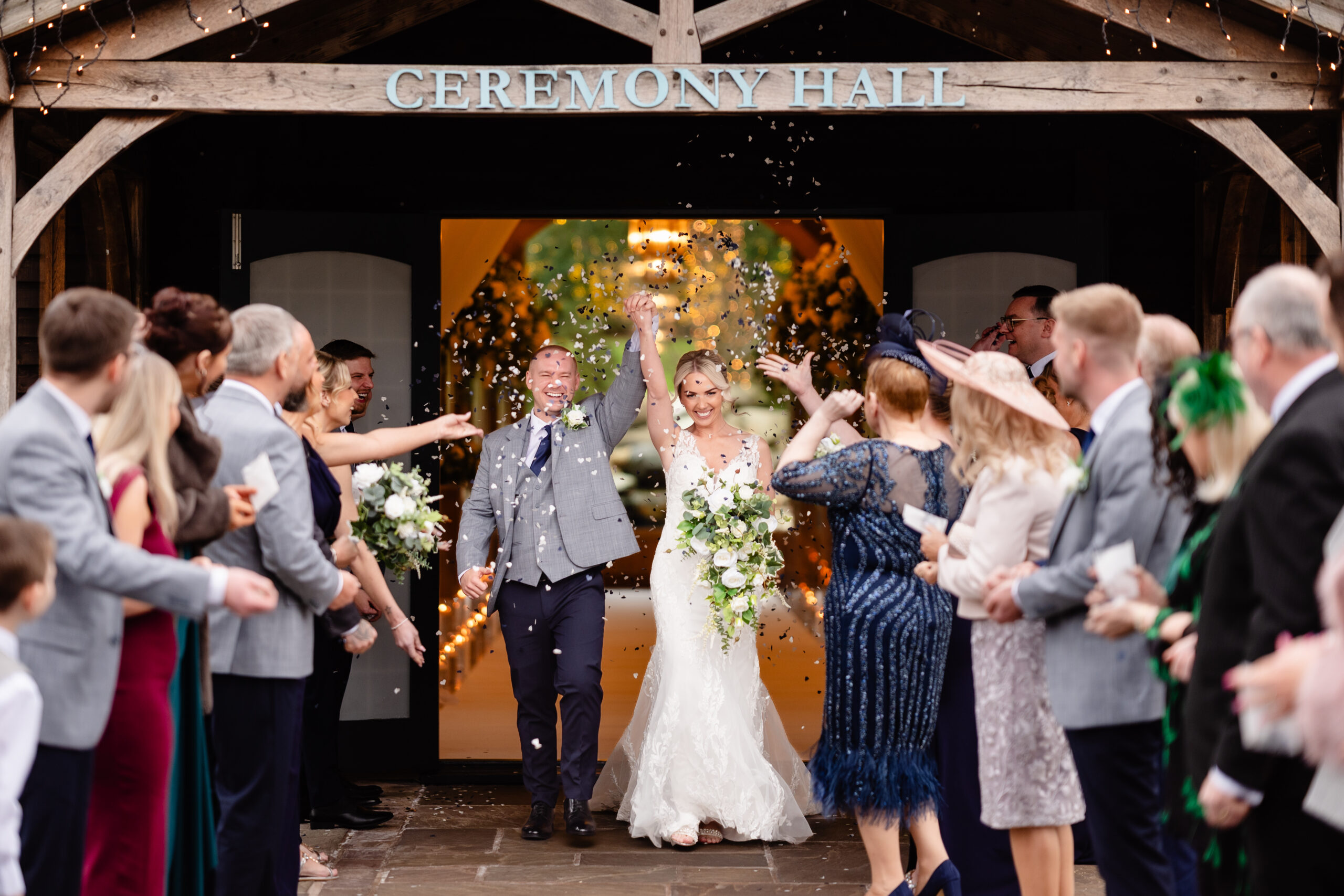 Bride and groom stepping out under the Ceremony Hall sign into a shower of confetti thrown by their guests, Colshaw Hall wedding