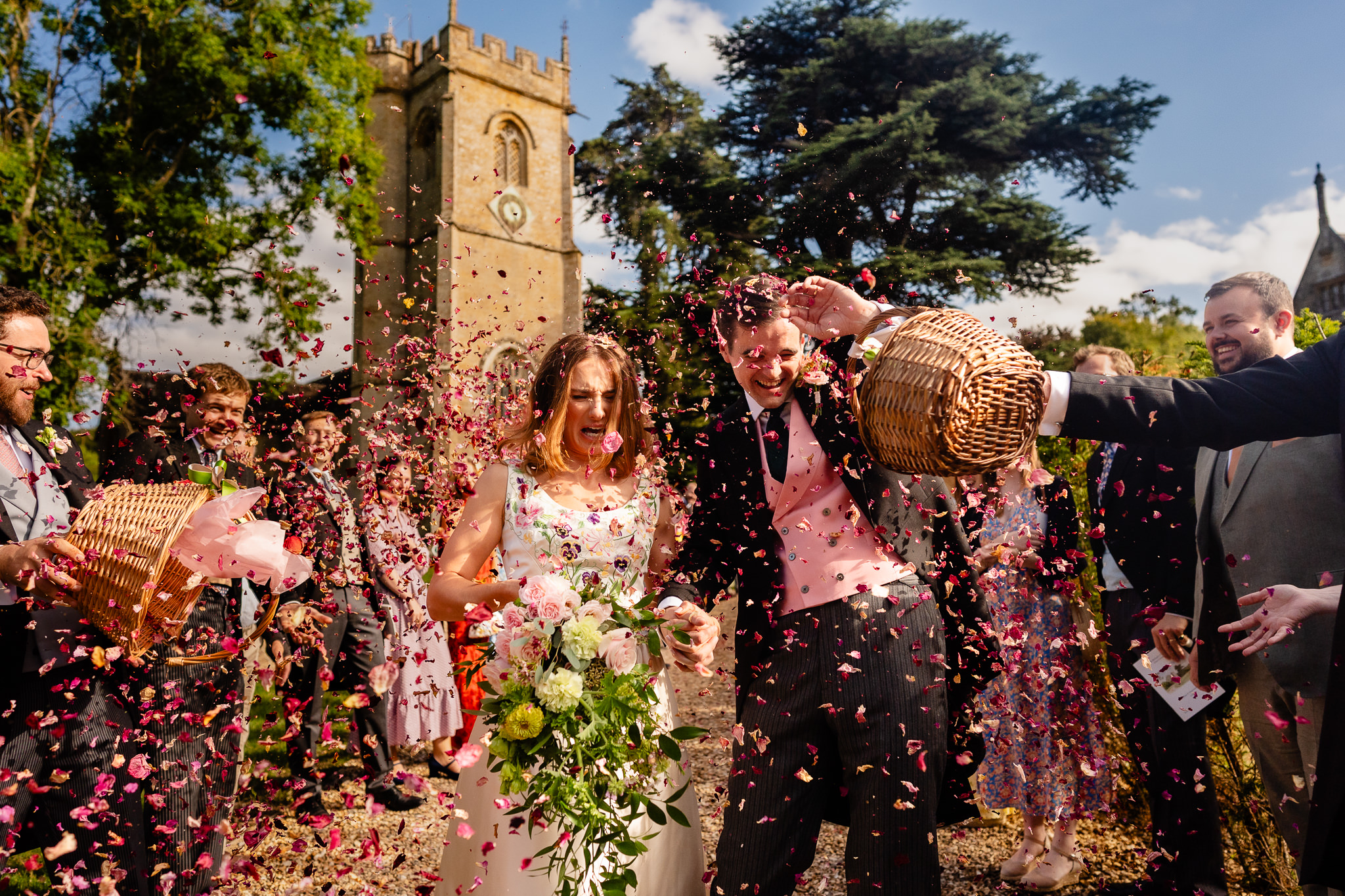 Guest tipping a whole basket of petal confetti over the newlyweds outside the church